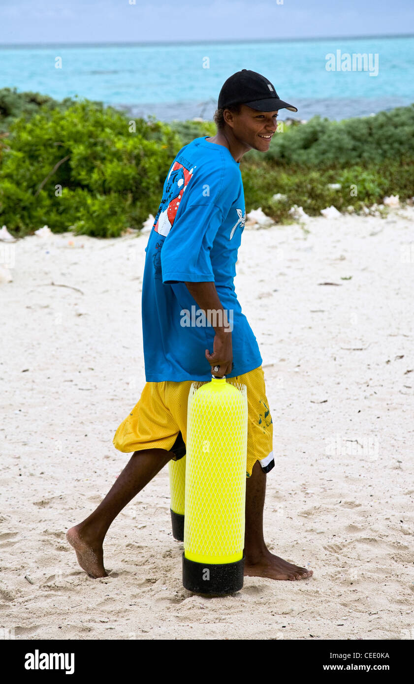 Lächelnde junge Mann trägt Tauchflaschen an einem Strand auf Glover es Reef Belize Stockfoto