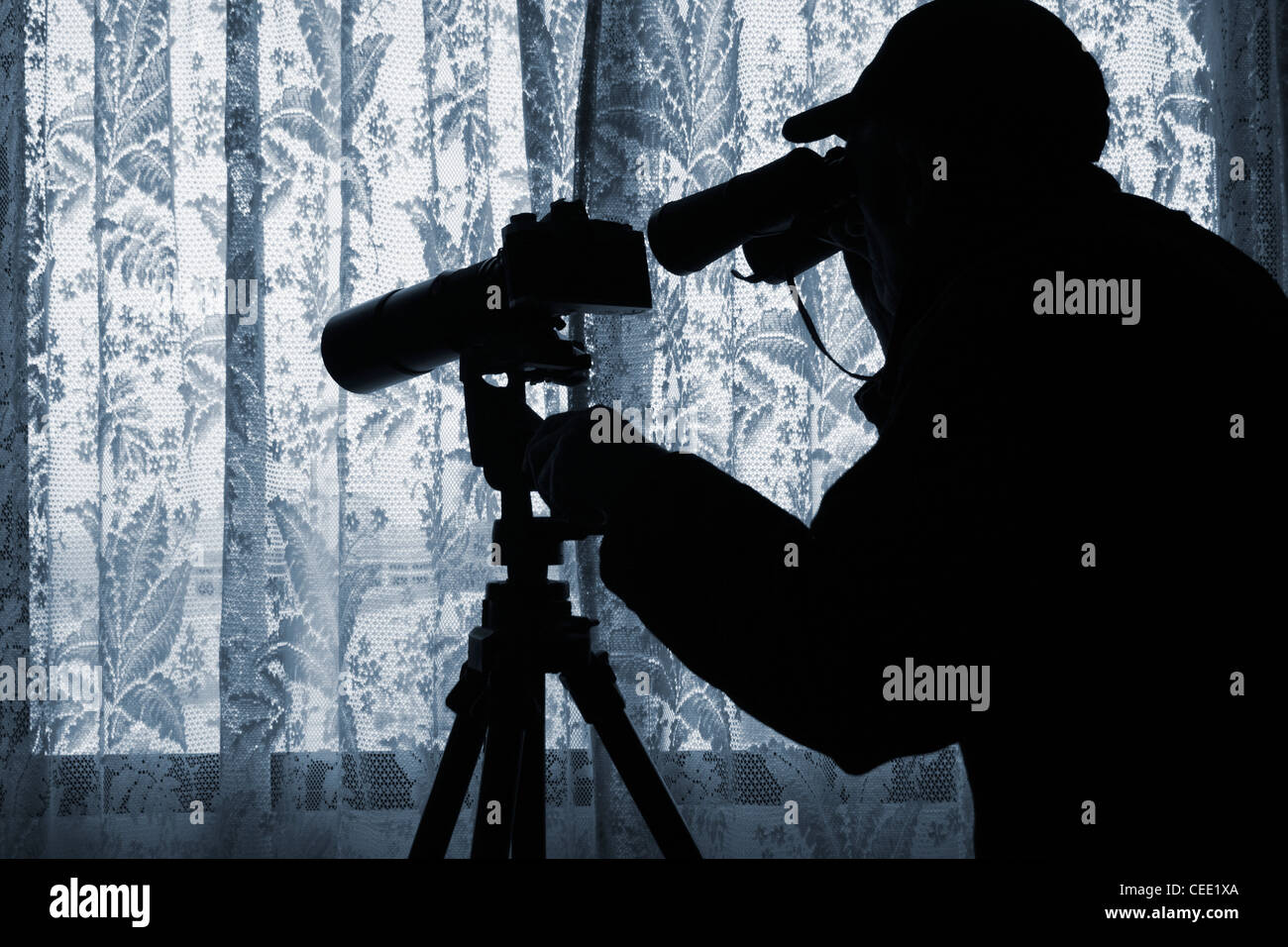 Mann mit Fernglas und Kamera mit Teleobjektiv auf Stativ Blick durch Gardinen. Foto von Model posierte. Stockfoto