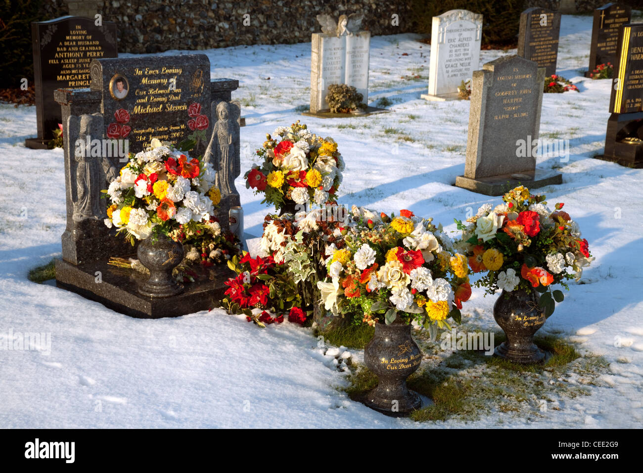 Ein Grab mit vielen Blumen im Speicher, im Winterschnee, Suffolk UK Stockfoto