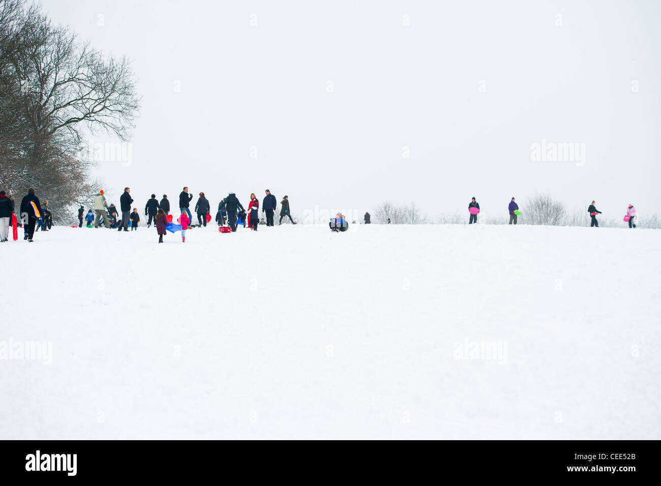 Eine Anzahl von Menschen auf einem Hügel im Schnee mit ihren Kindern und genießen die frische Schlitten fallen des Schnees in Essex, England. Stockfoto