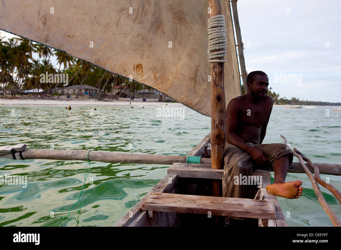 Zanzibari Mann sitzt in der Bögen von einer Dhau Segeln, im Meer vor dem Korallenriff in Bwejuu, Sansibar, Tansania Stockfoto