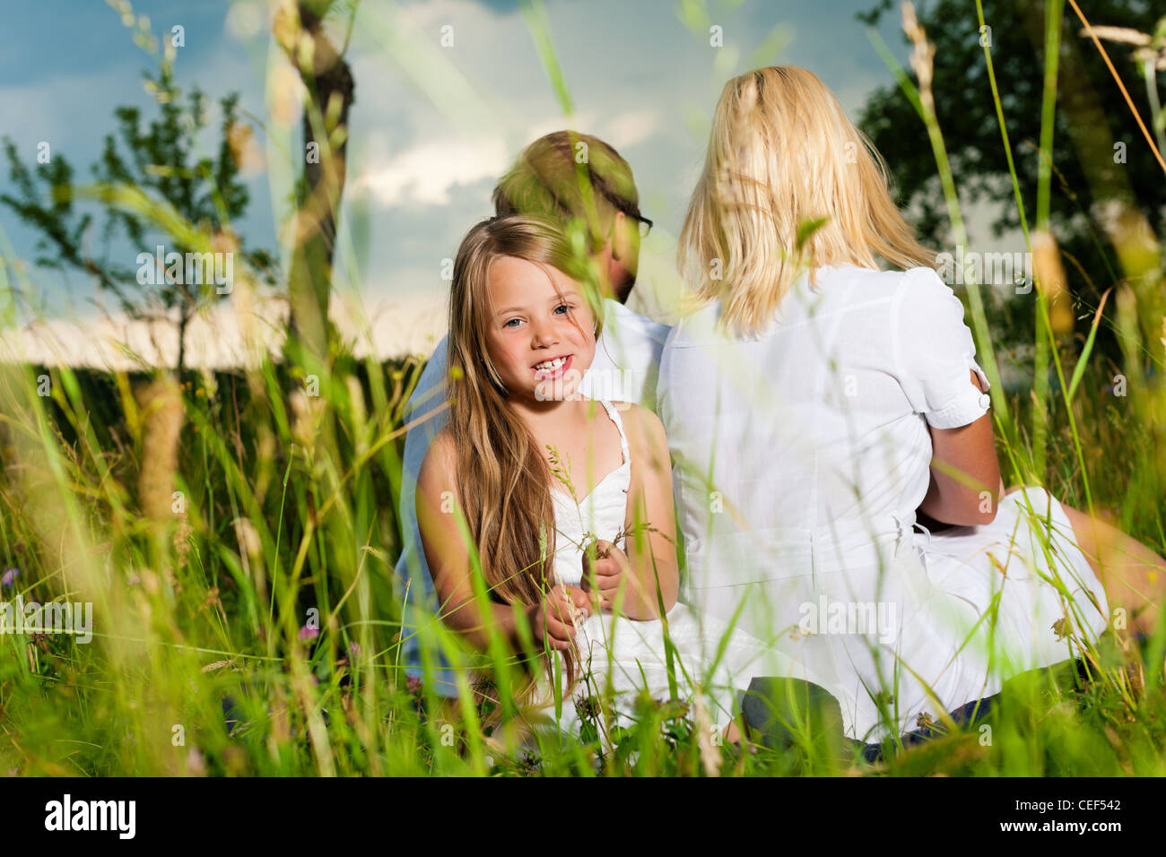 Glückliche Familie mit Tochter Mädchen sitzen auf einer Wiese im Sommer ...