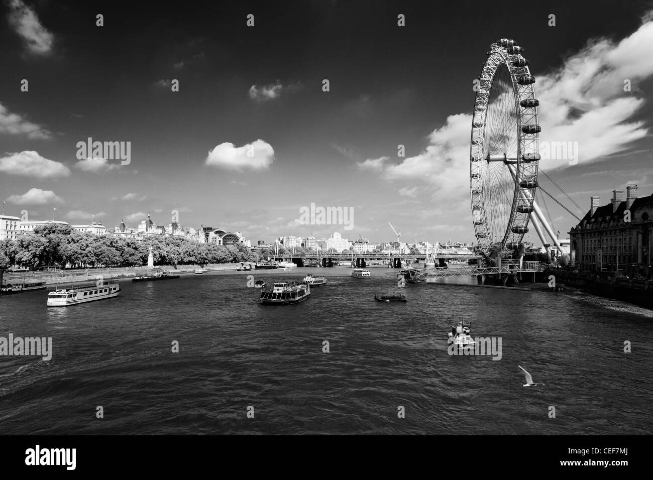 Das London Eye mit Charing Cross Station und Hungerford Bridge im Hintergrund, entnommen dem ein Boot auf der Themse Stockfoto