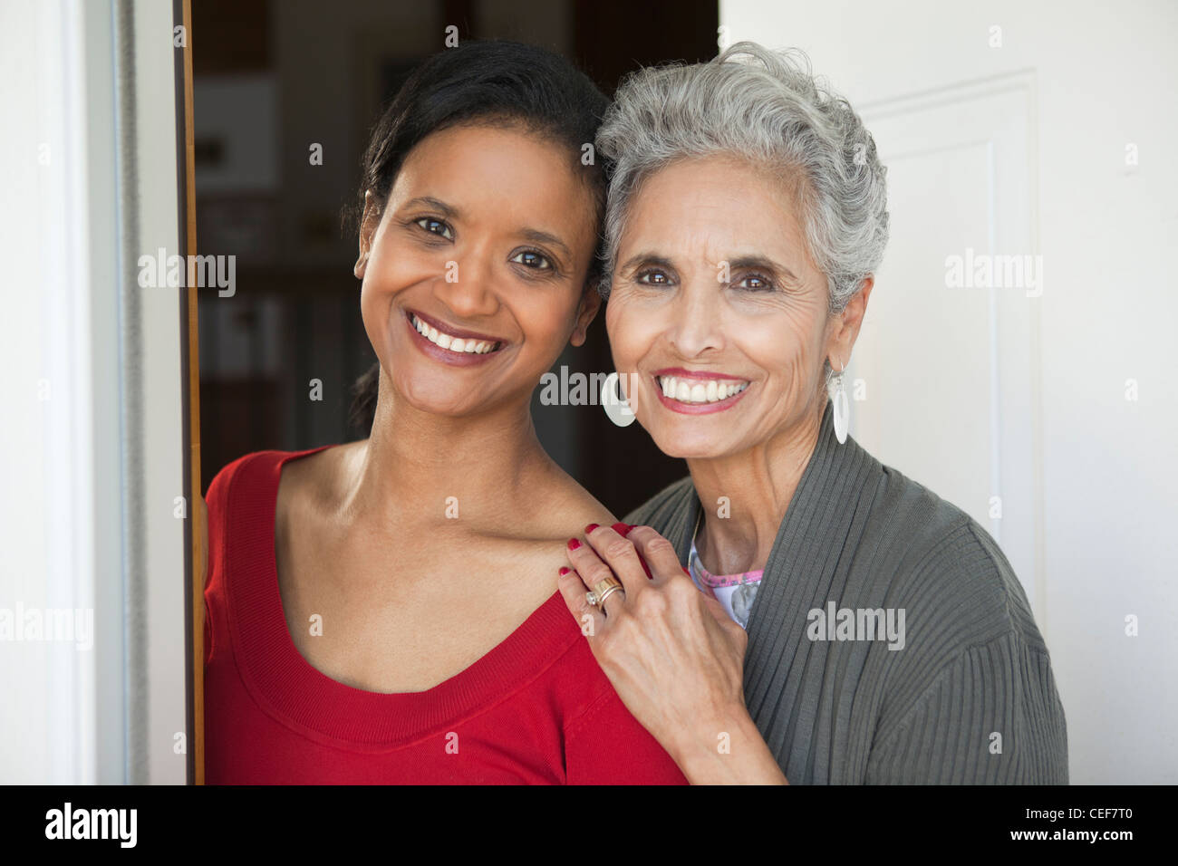 Schöne ältere Mutter und erwachsene Tochter lächelnd in die Kamera an der Haustür. Stockfoto