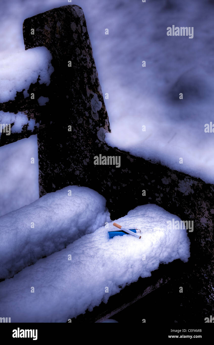 Zigarette und einer blauen leichter im Schnee auf eine Steinbank Stockfoto