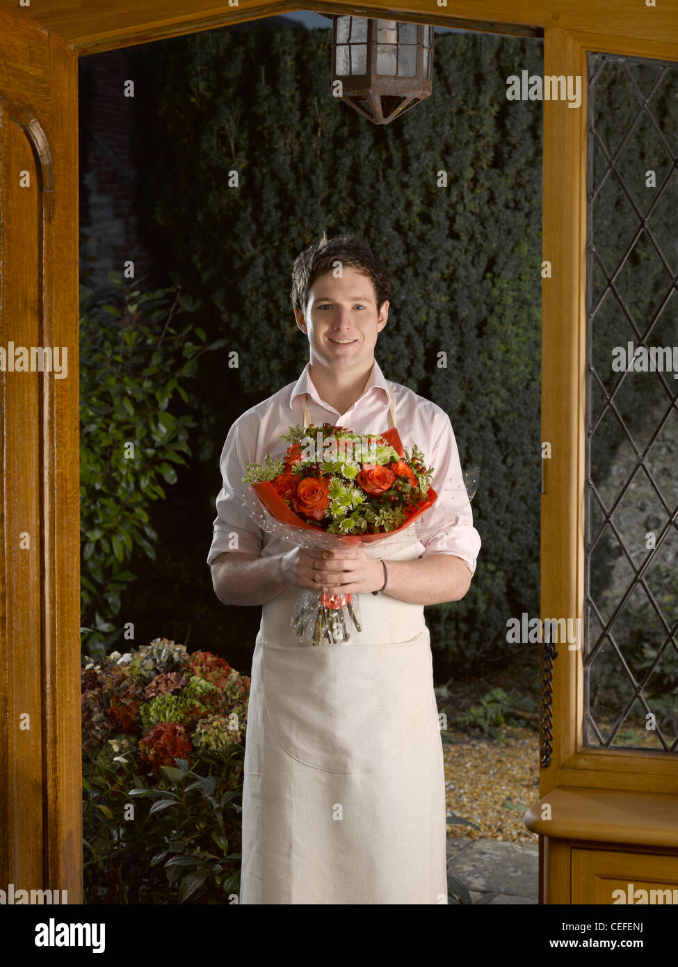 Mann in Schürze holding Bouquet in Tür Stockfoto