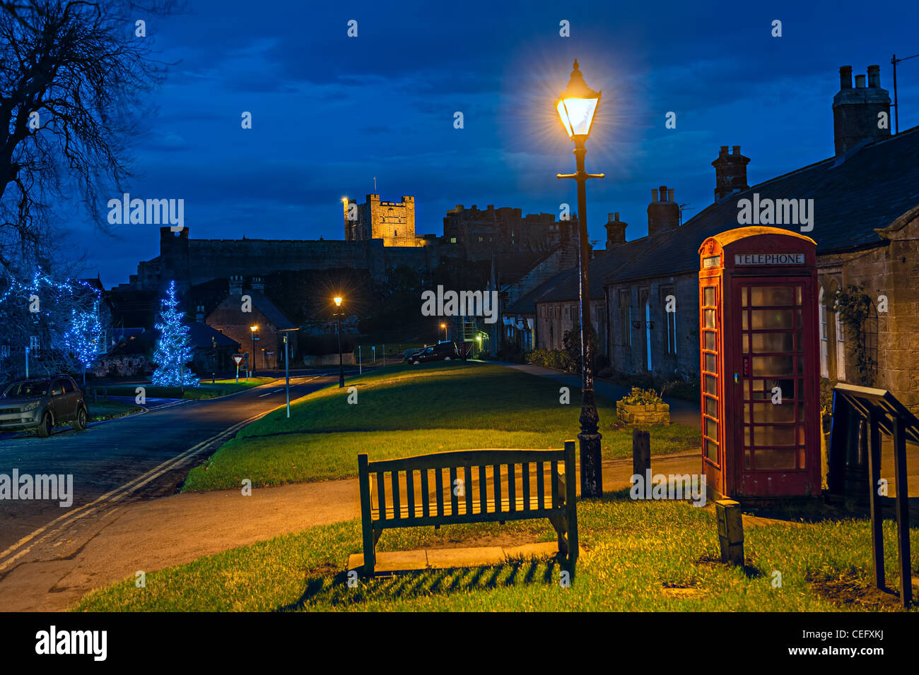 Bamburgh Dorf, Northumberland, England, UK, in der Abenddämmerung mit Bamburgh Castle im Hintergrund, zu Weihnachten Stockfoto