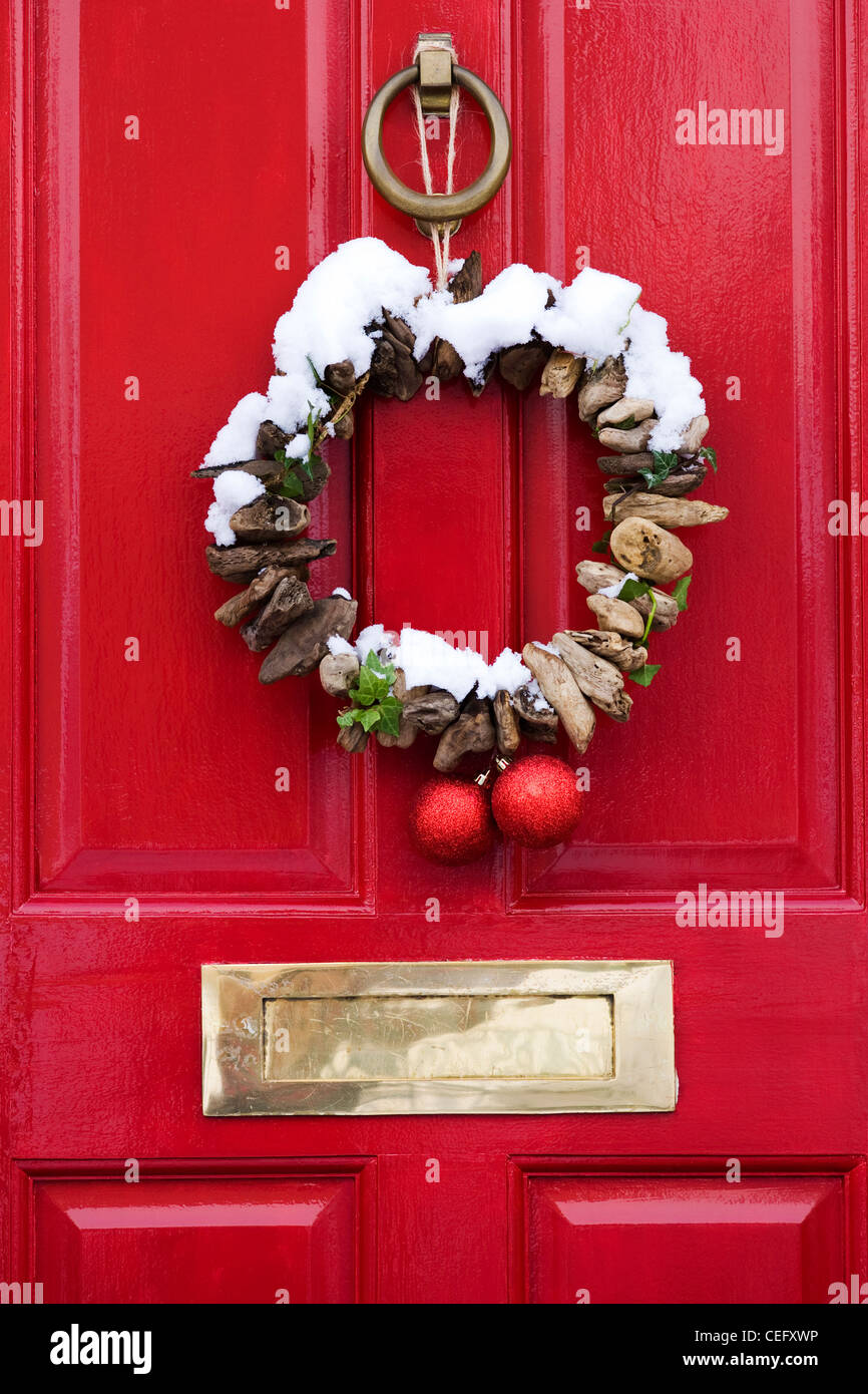 Dekorative Treibholz Weihnachtskranz an einem roten Eingangstür hängen. Stockfoto