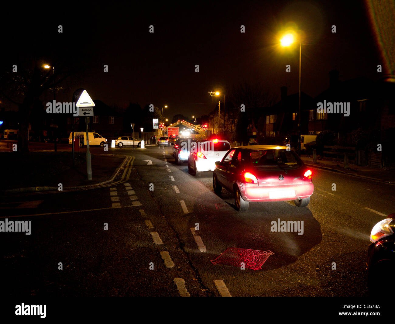Autos in der Nacht an Motspur Park Station in SW London England an einem Bahnübergang warten Stockfoto