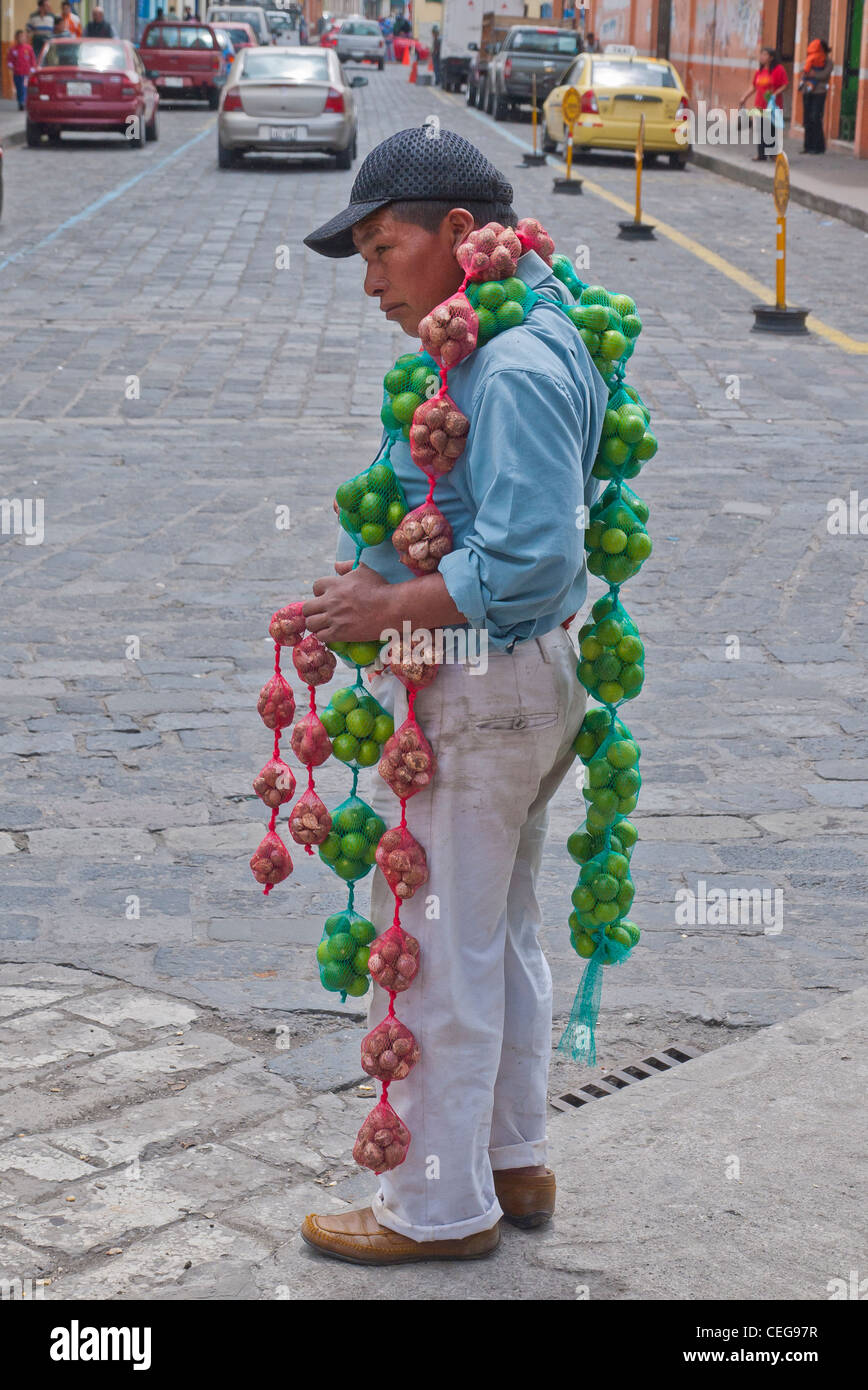 30-40 Jahre alten Straßenverkäufer trägt ein Fäden gewebte Netze mit Limetten und anderen Produkten für den Verkauf in Latacunga, Ecuador. Stockfoto