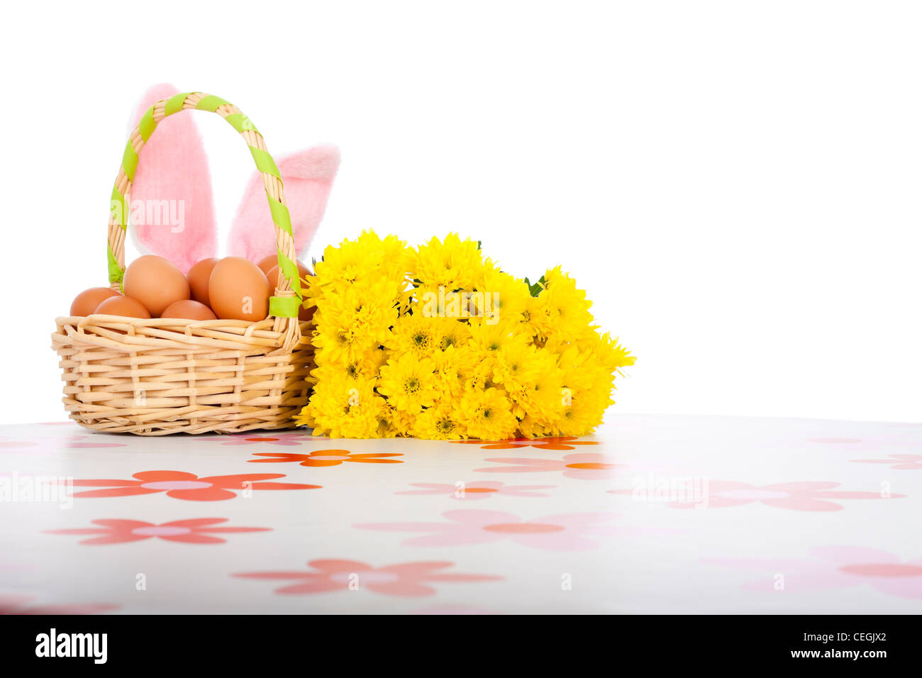 Osterkorb mit Eiern, gelben Blüten und rosa Hasenohren, isoliert auf weißem Hintergrund. Stockfoto