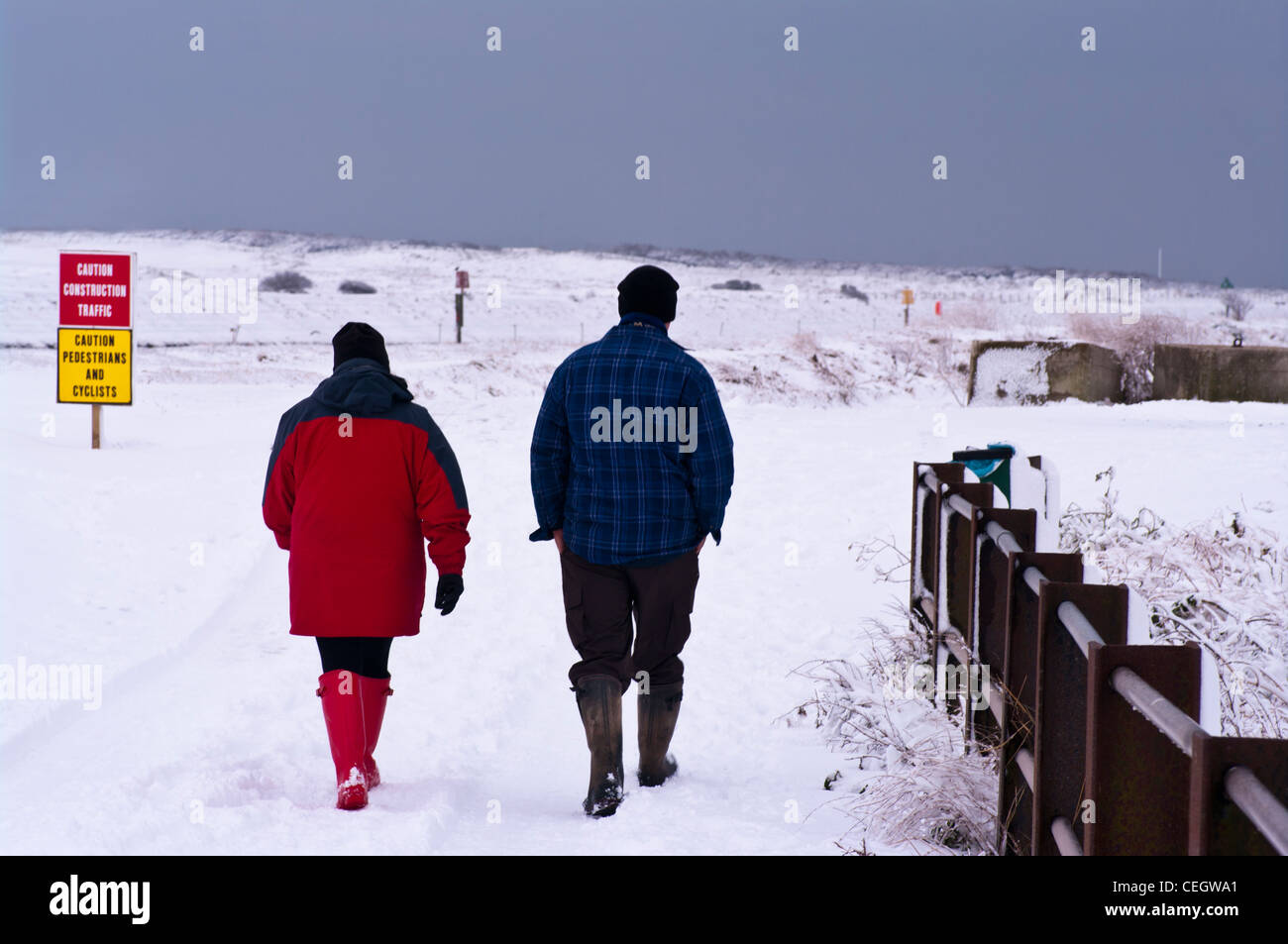 Rückseitige Ansicht von hinten von Mann und Frau Menschen paar zu Fuß durch den Schnee tragen Mäntel Mützen und Wellington Boots UK Stockfoto