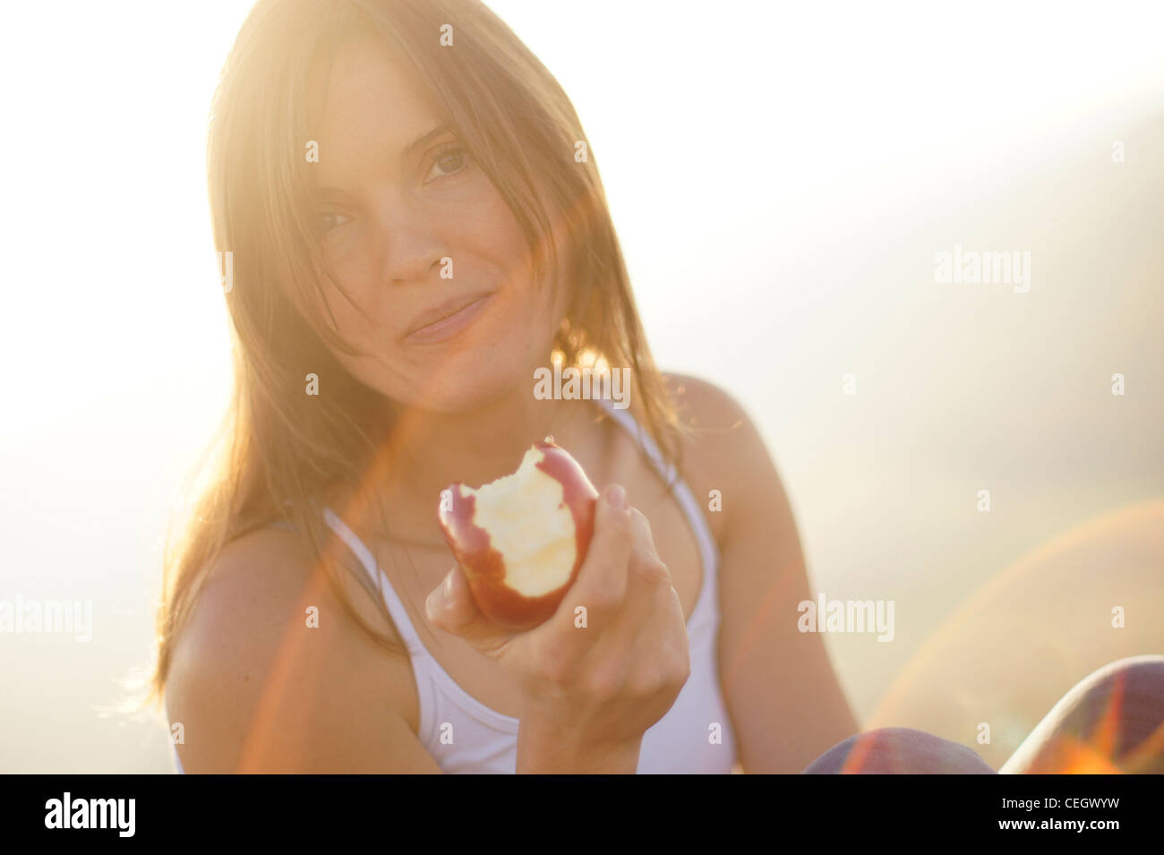 Schöne junge Frau, die einen saftigen roten Apfel zu essen, im schönen goldenen Licht der untergehenden Sonne Stockfoto