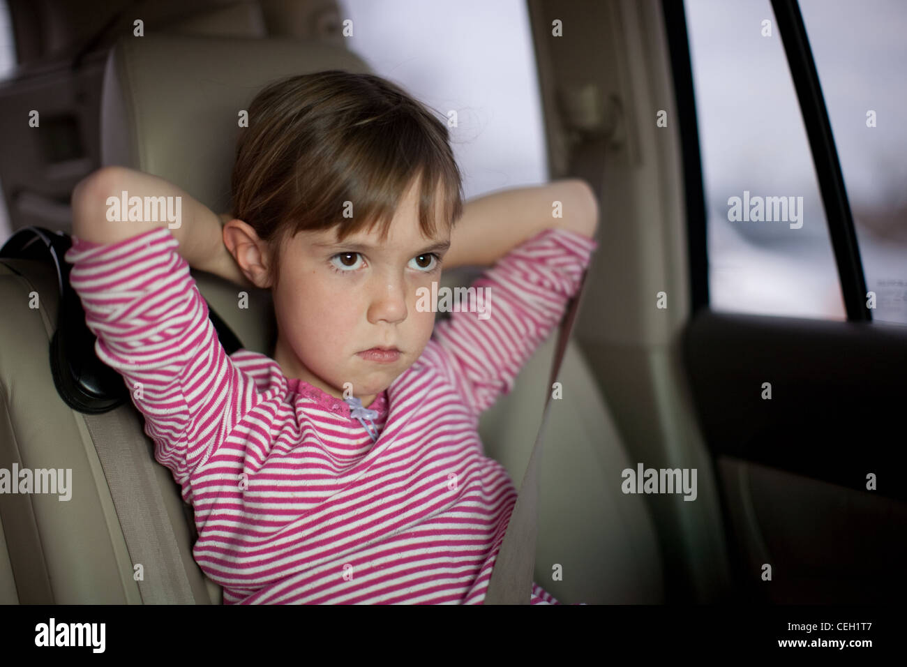 Sechs Jahre altes Mädchen sitzen in einem Auto mit Armen hinter dem Kopf, schmollend. Ernst, Heck, Enttäuschung. Stockfoto