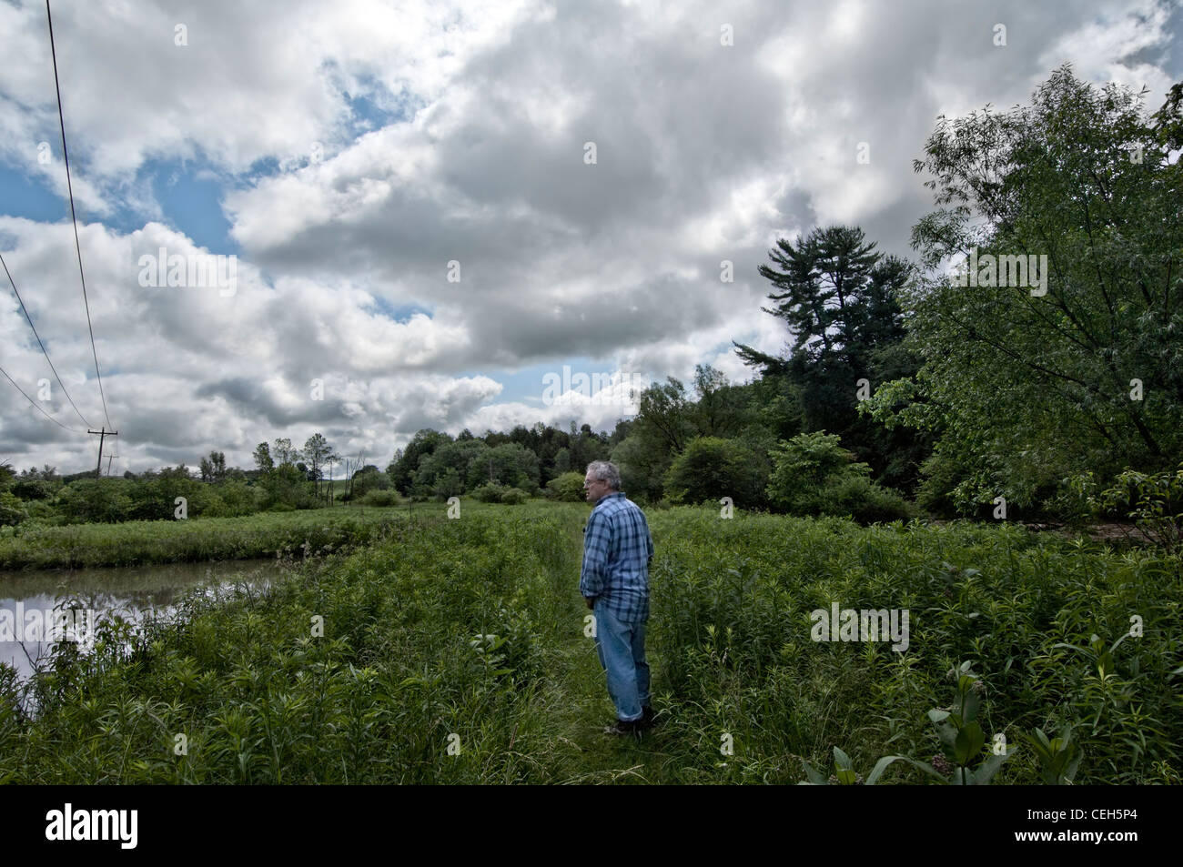 ein Mann steht allein in einem Feld in der Nähe von einem Teich Stockfoto