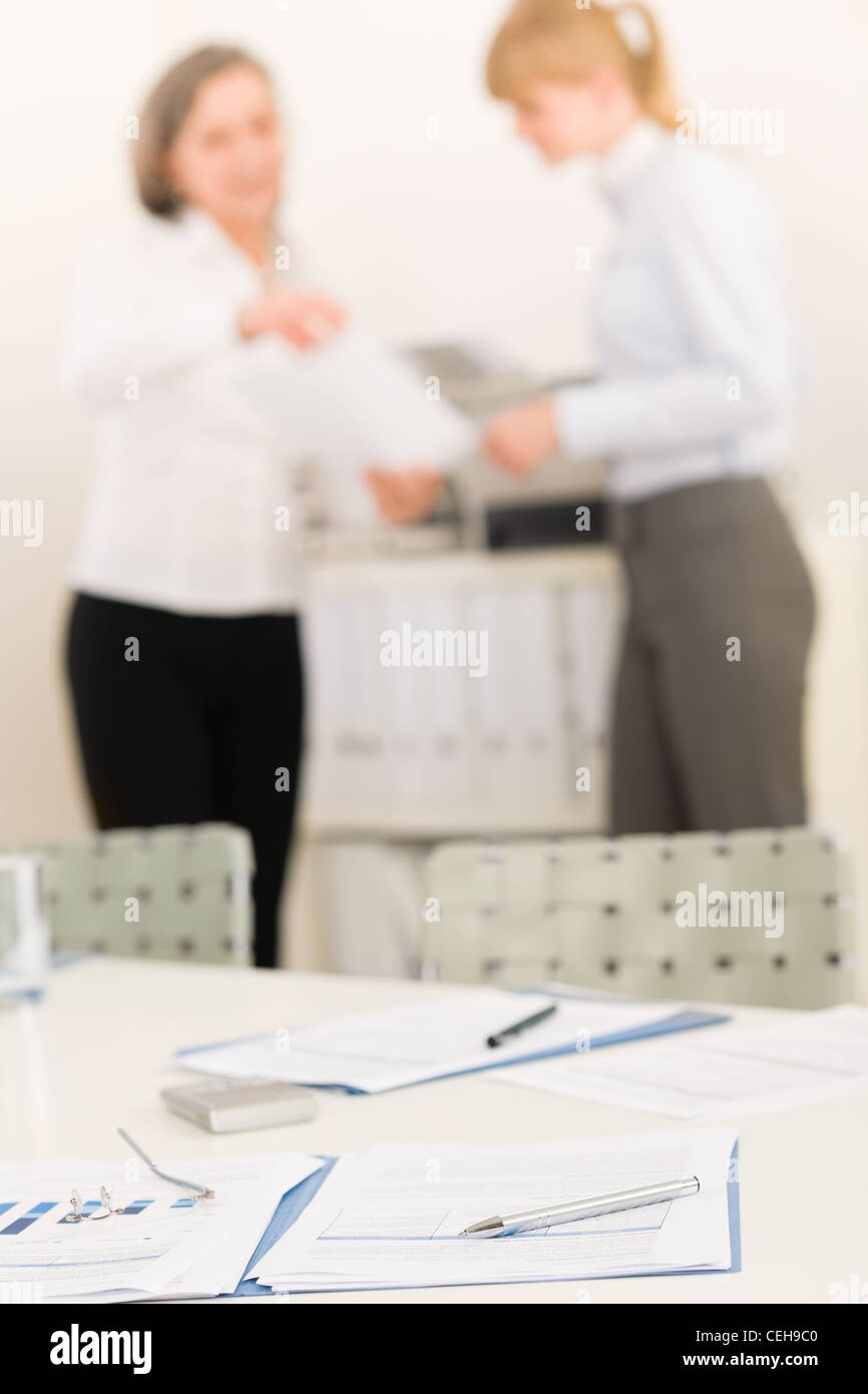 Bürobedarf auf Tisch - zwei Geschäftsfrauen aus dem Fokus Stockfoto