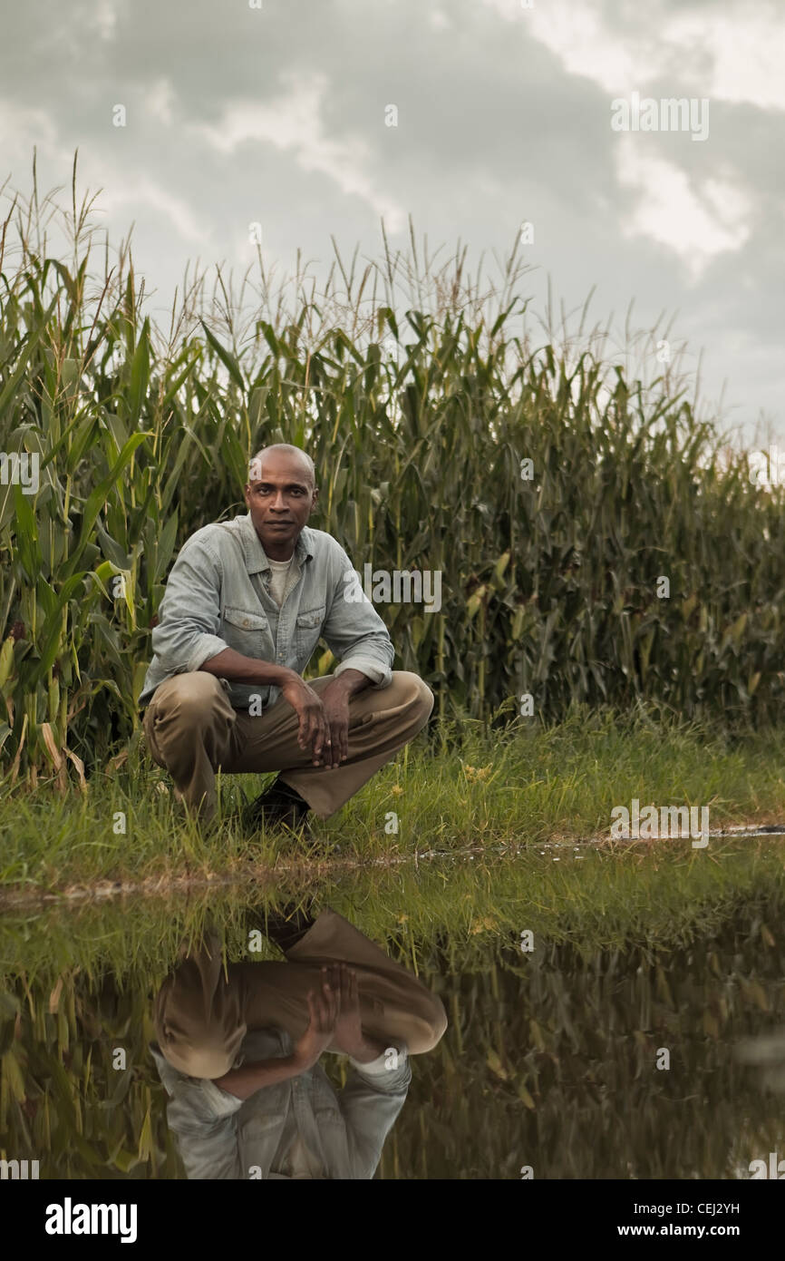 African American Farmer hocken in der Nähe von Wasser und Pflanzen Stockfoto