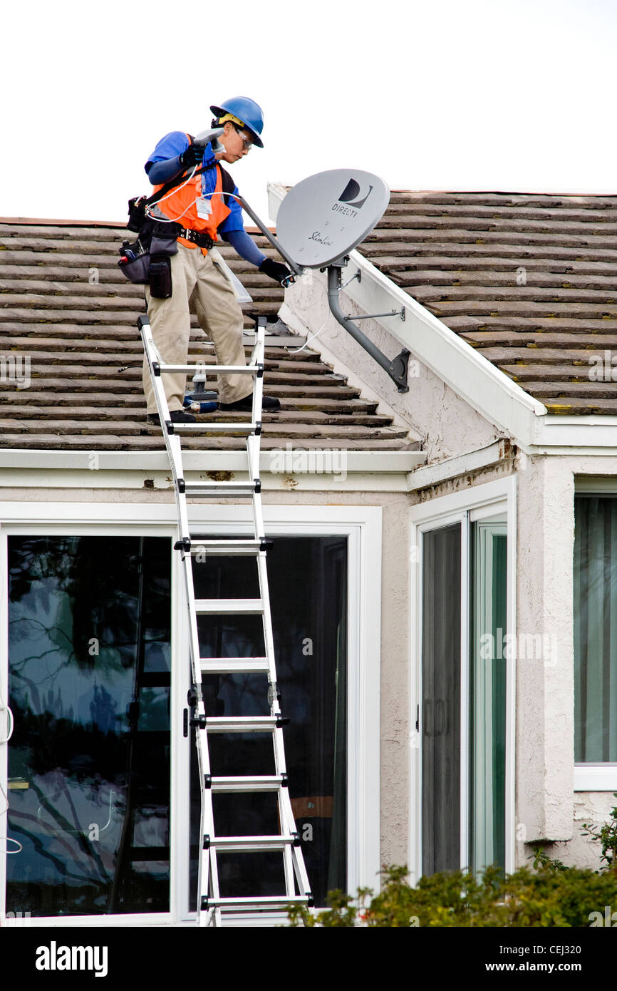 Ein Techniker installiert eine Satellitenschüssel auf dem Dach eines neu erworbenen Hauses in Laguna Niguel, CA Stockfoto