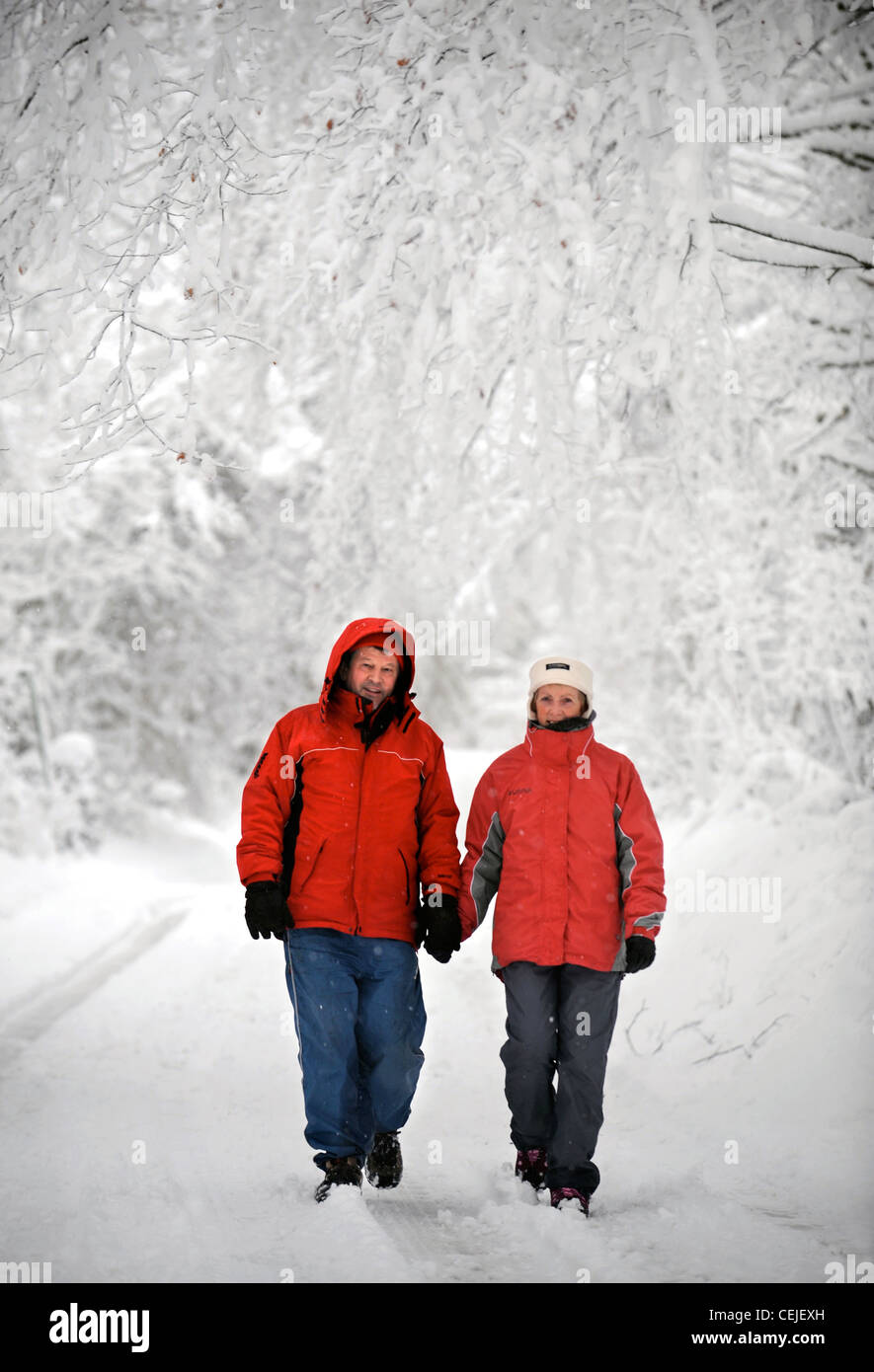 Ein paar in passenden roten Wintermäntel zu Fuß in einer Cotswold-Gasse in Schneeverhältnissen UK Stockfoto