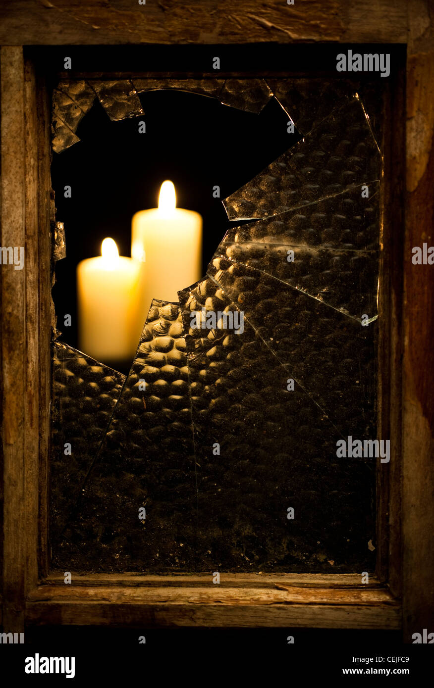 Ein zerbrochenes Glas-Fensterscheibe mit brennenden Kerzen Stockfoto