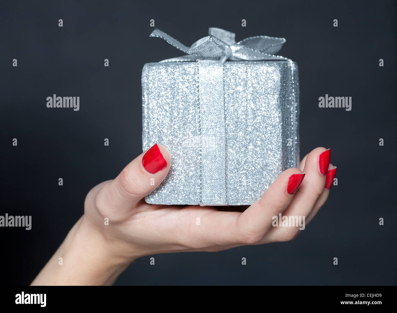 Weibliche Hand mit rot lackierten Fingernägel, hält eine silberne Weihnachtsgeschenk Stockfoto