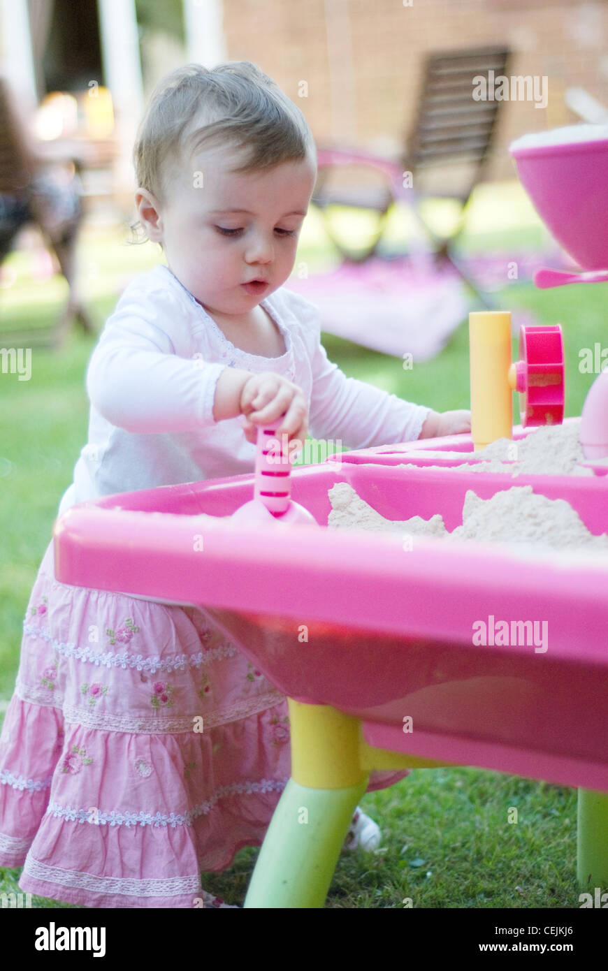 Ein weibliches Baby Fait Haar, trägt einen weißen Top und rosa Rock, spielen Sand im Garten, ernsten, blickte Joel Penn Stockfoto