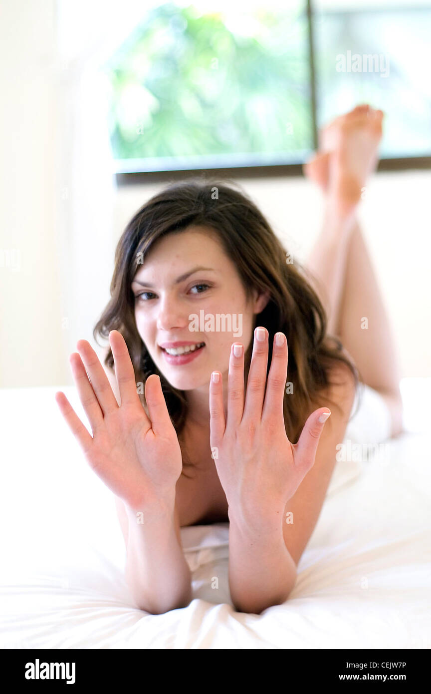 Weibchen mit brünette Haare, die Verlegung auf den Bauch auf einem Bett hält ihr die Hände an der Kamera Stockfoto