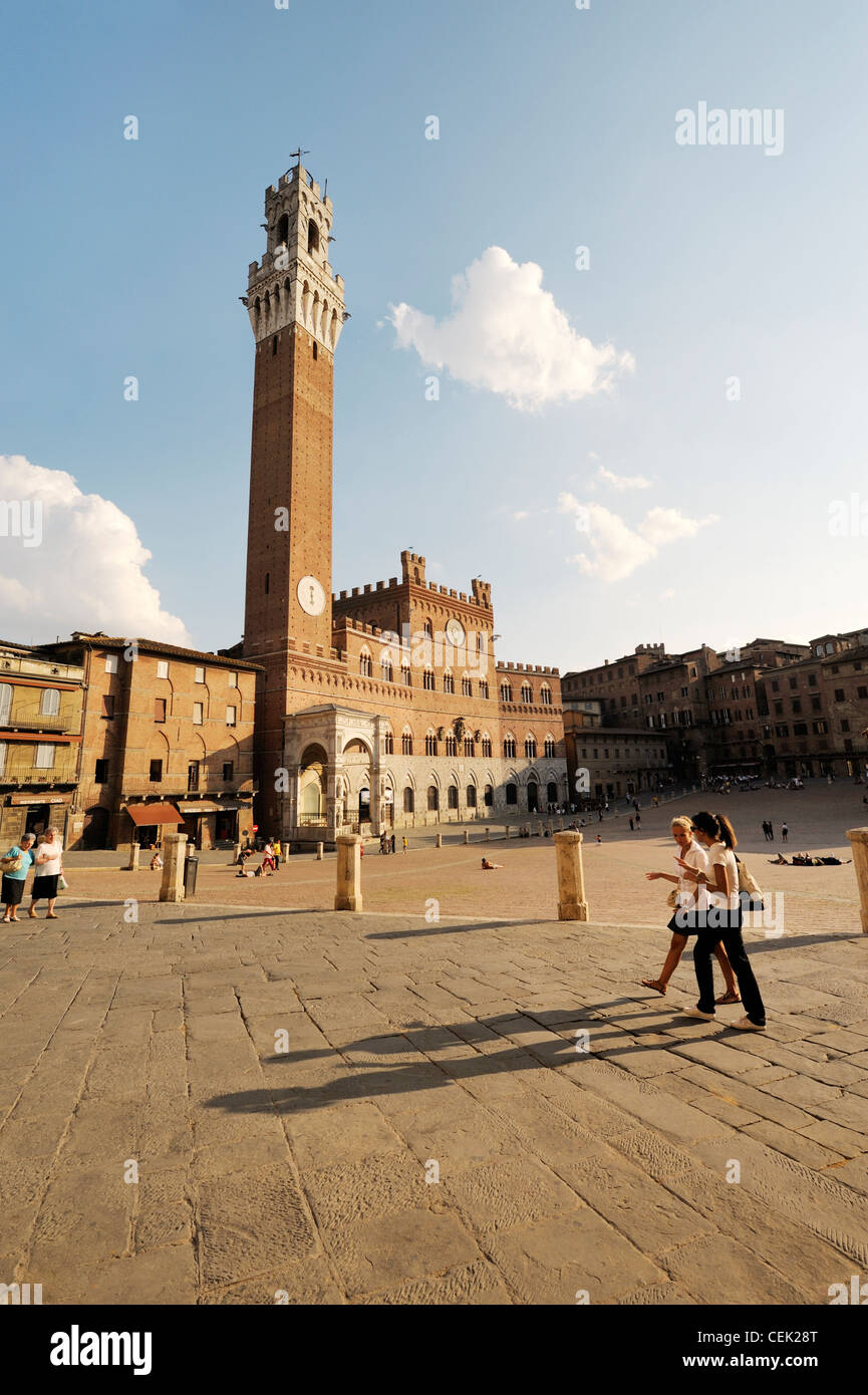 Touristen auf der Piazza del Campo, dem zentralen Platz der Stadt Siena, Toskana, Italien. Torre del Mangia Turm erhebt sich hinter Stockfoto