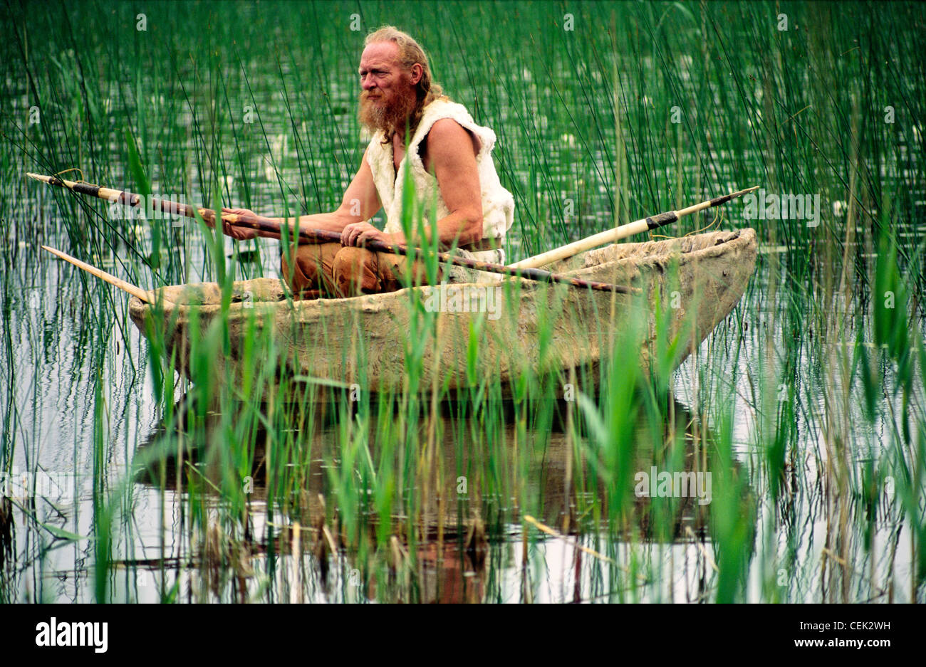 Jungsteinzeit Re-enactment. Stein alter Mann mit Fisch Spieß in Tier coracle Boot verstecken auf Reed ufer See. kilmartin, Schottland, Großbritannien Stockfoto