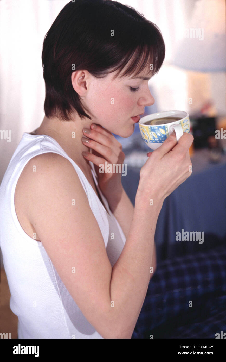 Profil von Weibchen mit kurze brünette Haare mit weißen V Hals Weste trinken Schwarztee mit Zitrone Hand Hals Augen geschlossen Stockfoto