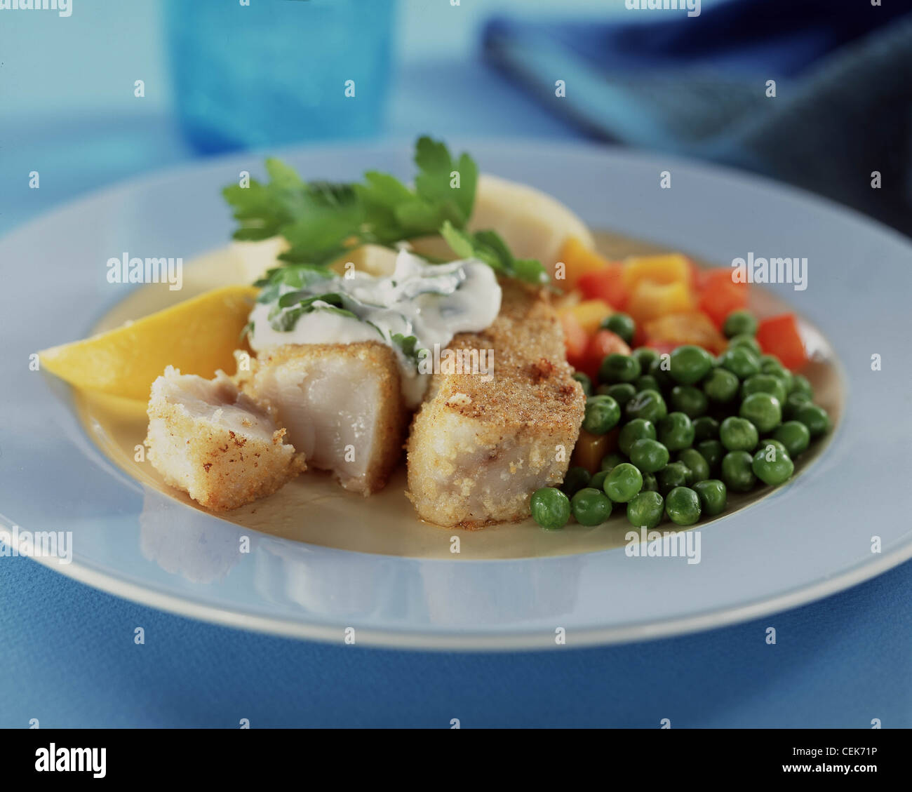 Blau-Creme Platte zwei Stücke von weißen Fisch beschichtete Brot Krümel Crème Fraiche-Kräuter-Sauce auf Top Erbsen gekochte Kartoffeln in Würfel geschnitten Stockfoto