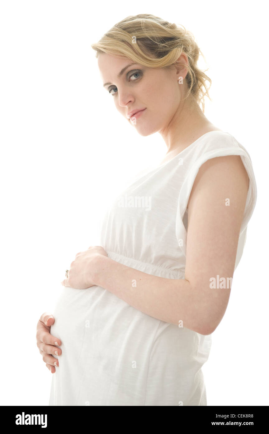 Schwangeres Frauen blondes Haar gebunden zu Pferdeschwanz, trägt ein weißes Kleid, stehend durch die Fenster Hände auf Bauch, ernsten, auf der Suche Stockfoto