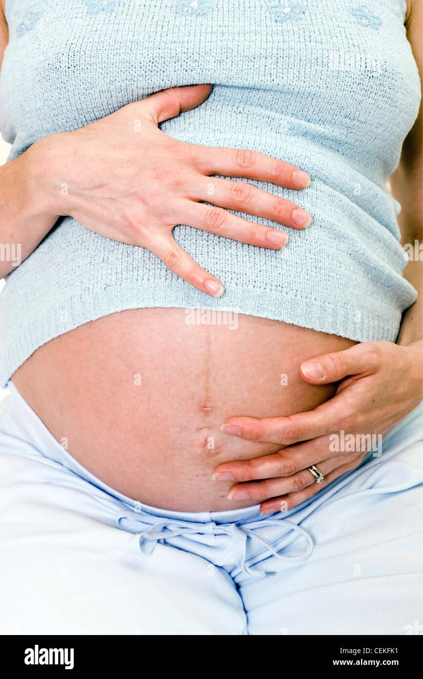 Nahaufnahme von Weibchen tragen blasse blaue Weste und Hose, sitzt auf Bett hochschwangere Magen, direkt in die Kamera halten Stockfoto