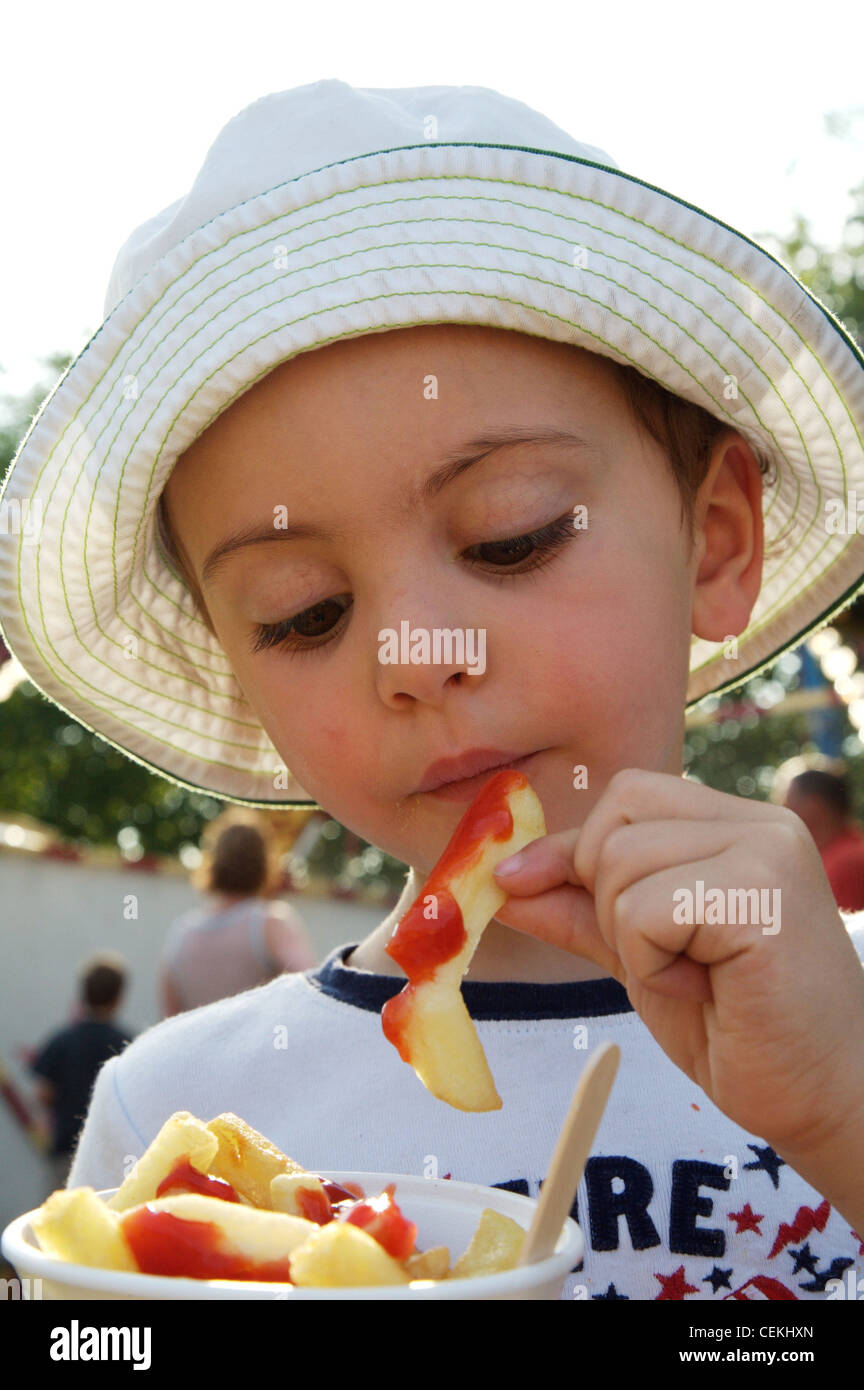 Männliches Kind, dunkelblondes Haar, weiße Sonnenhut, grüne Nähte, weiß-T-Shirt, blau Trim, hält Kegel Chips Tomaten-ketchup Stockfoto