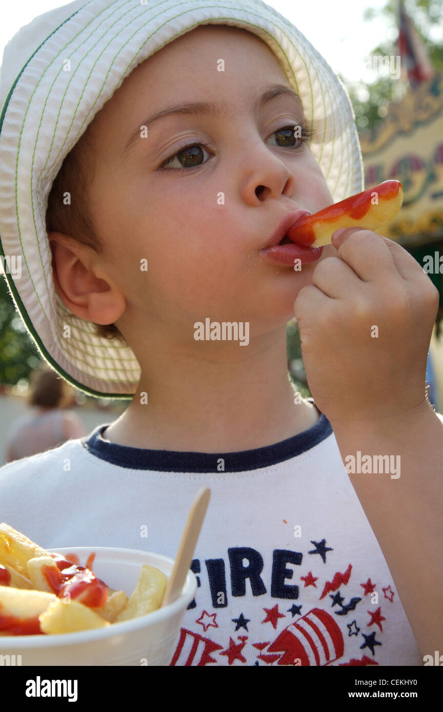 Männliches Kind, dunkelblondes Haar, weiße Sonnenhut, grüne Nähte, weiß-T-Shirt, blau Trim, hält Kegel Chips Tomaten-Ketchup, Stockfoto