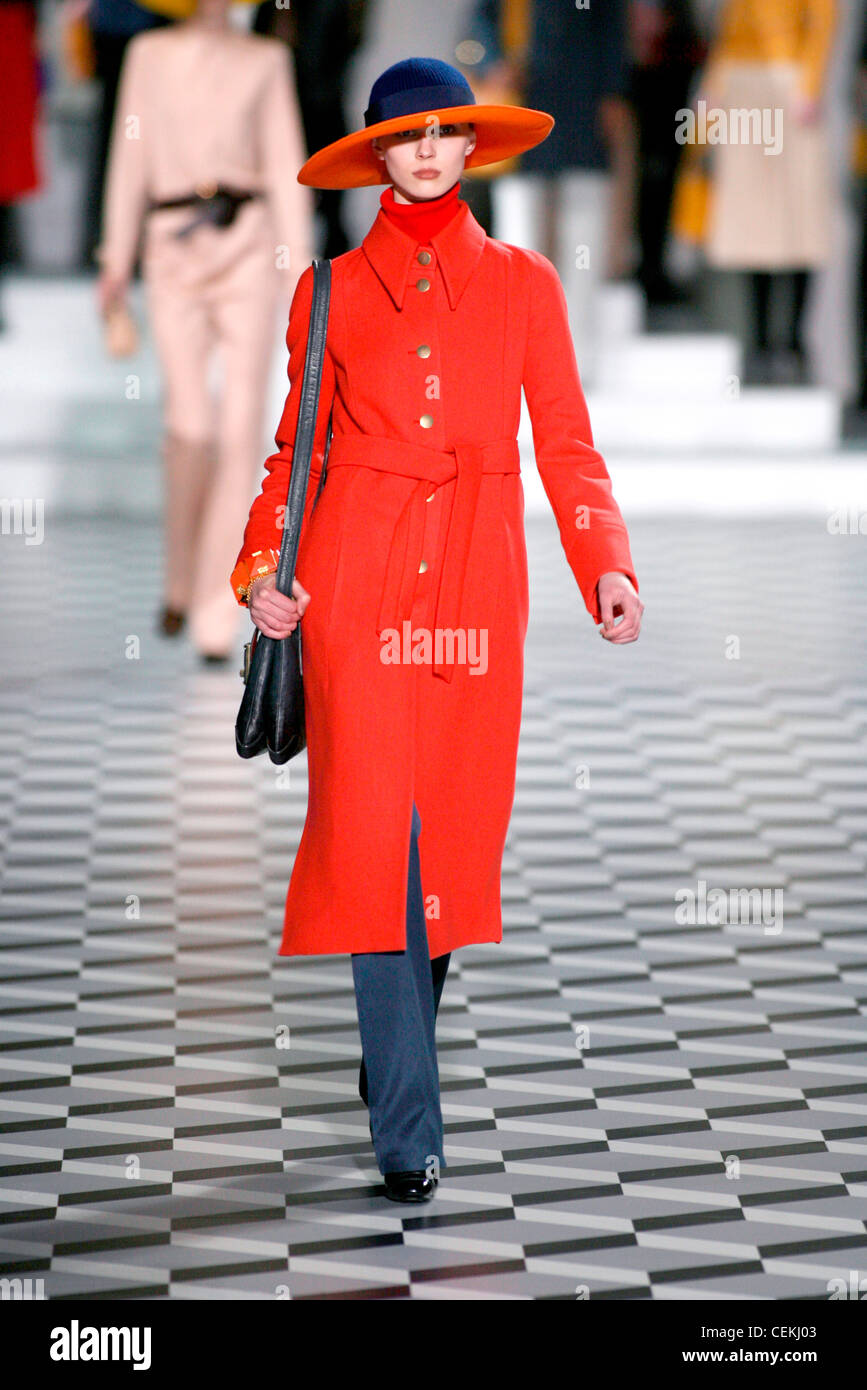 Model Olga Sherer tragen blaue Filzhut sehr breit orange Rand, rote Rollkragen unter roter Wolle Mantel Gürtel und Messing-Tasten über Stockfoto