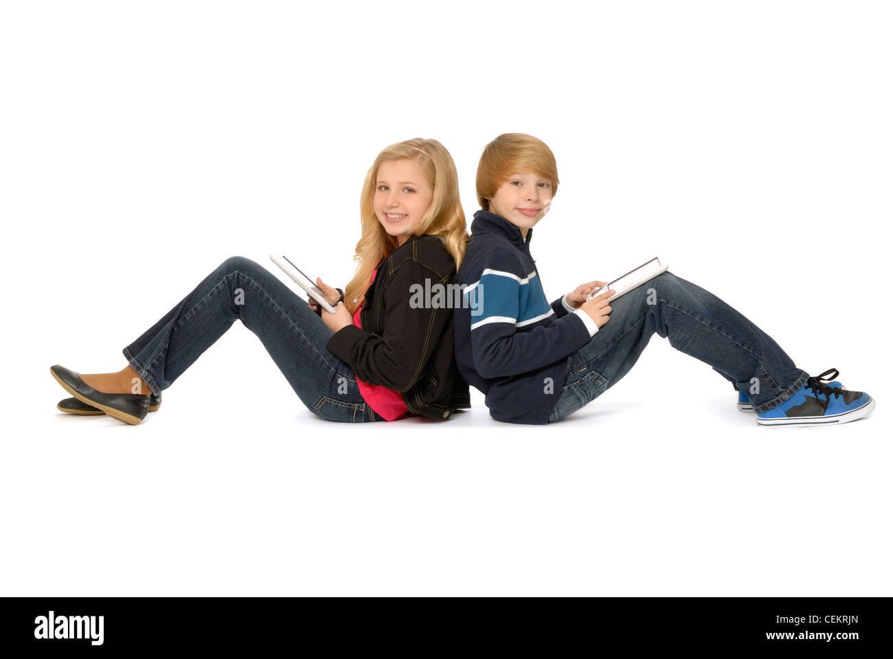 Zehn Jahre altes Mädchen und elf Jahre alten Jungen, Geschwister, sitzen Rücken an Rücken mit Tablet-PCs und lächelnd. Stockfoto