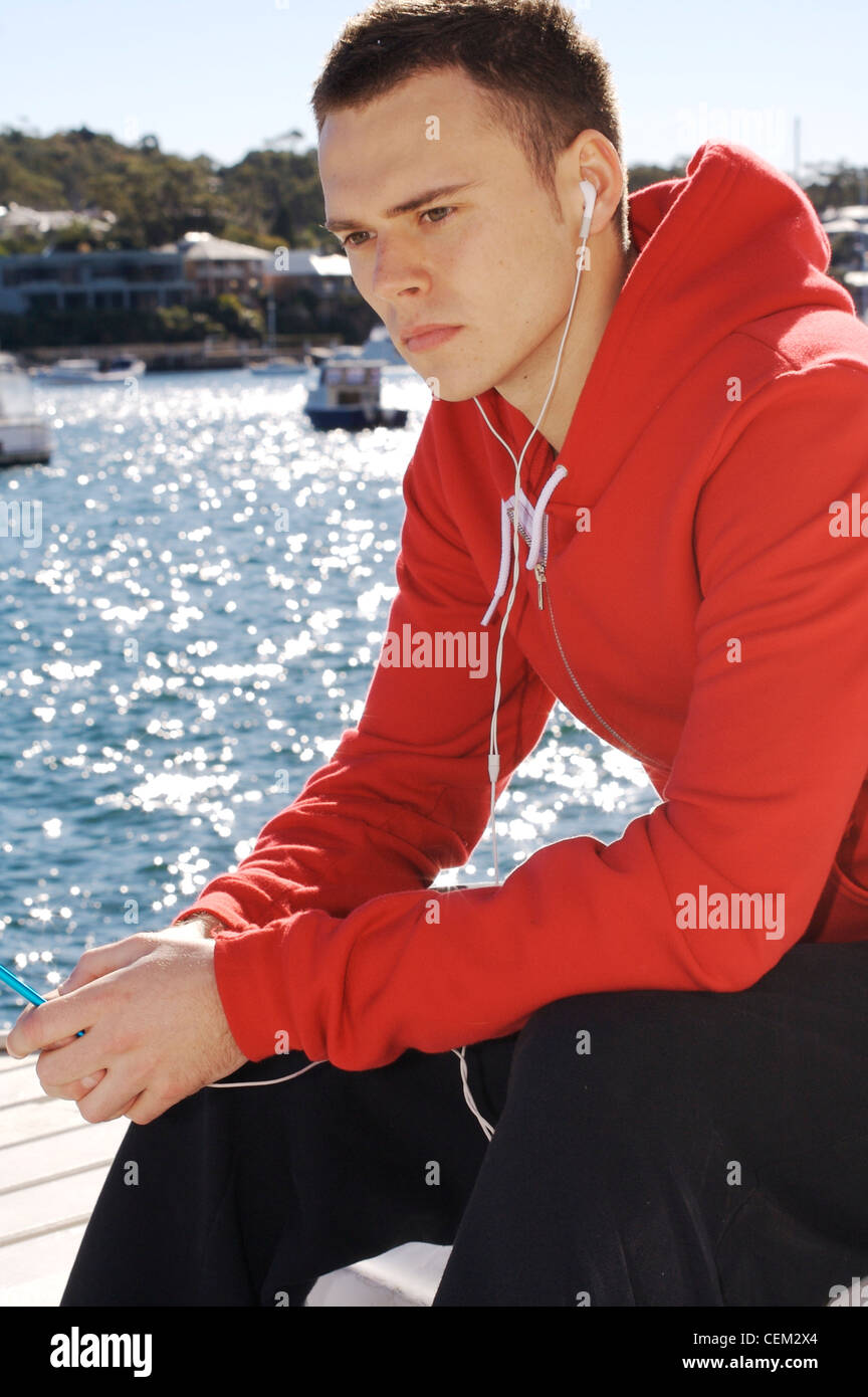Männlichen kurze brünette Haare, trägt ein rotes Sweatshirt mit Kapuze und schwarzen Trainingsanzug Böden, hält eine i pod mp Spieler beide Hände Stockfoto