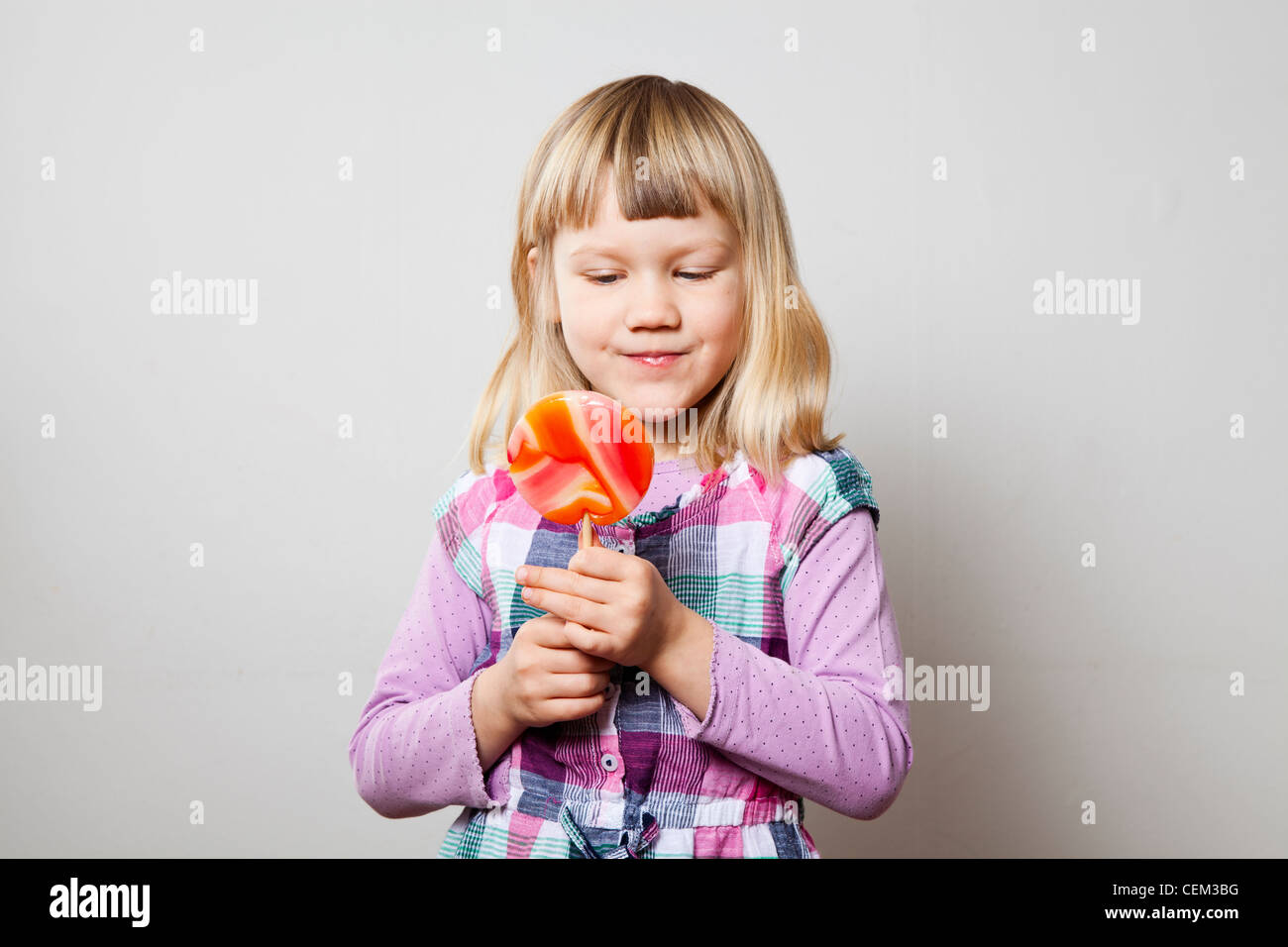 Niedliche kleine Mädchen mit einem großen orangefarbenen Lutscher. Studio gedreht. Stockfoto