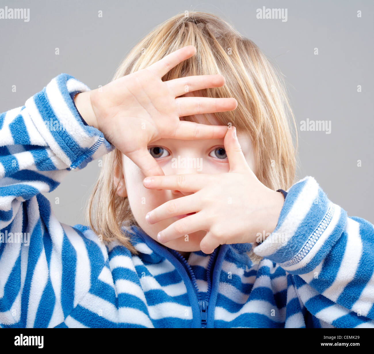 Junge mit langen blonden Haaren, die durch einen Finger Frame - isoliert auf grau Stockfoto