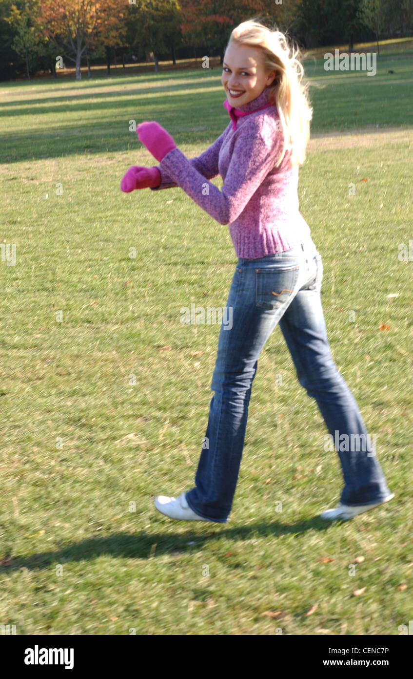 Weibliche blonde lange Haare tragen lila Neck Pullover und Jeans weiß Trainer leuchtend rosa Schal und Handschuhe zu Fuß über Rollen Stockfoto