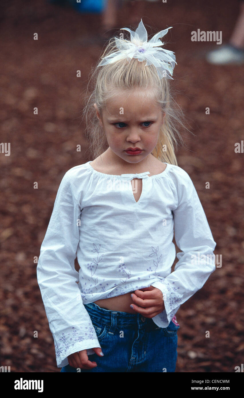 Weibliches Kind blonde Haare aus Gesicht in weiß Blume Haarband tragen weiße  Bluse und Jeans Nägel lackiert blau berühren Magen Stockfotografie - Alamy