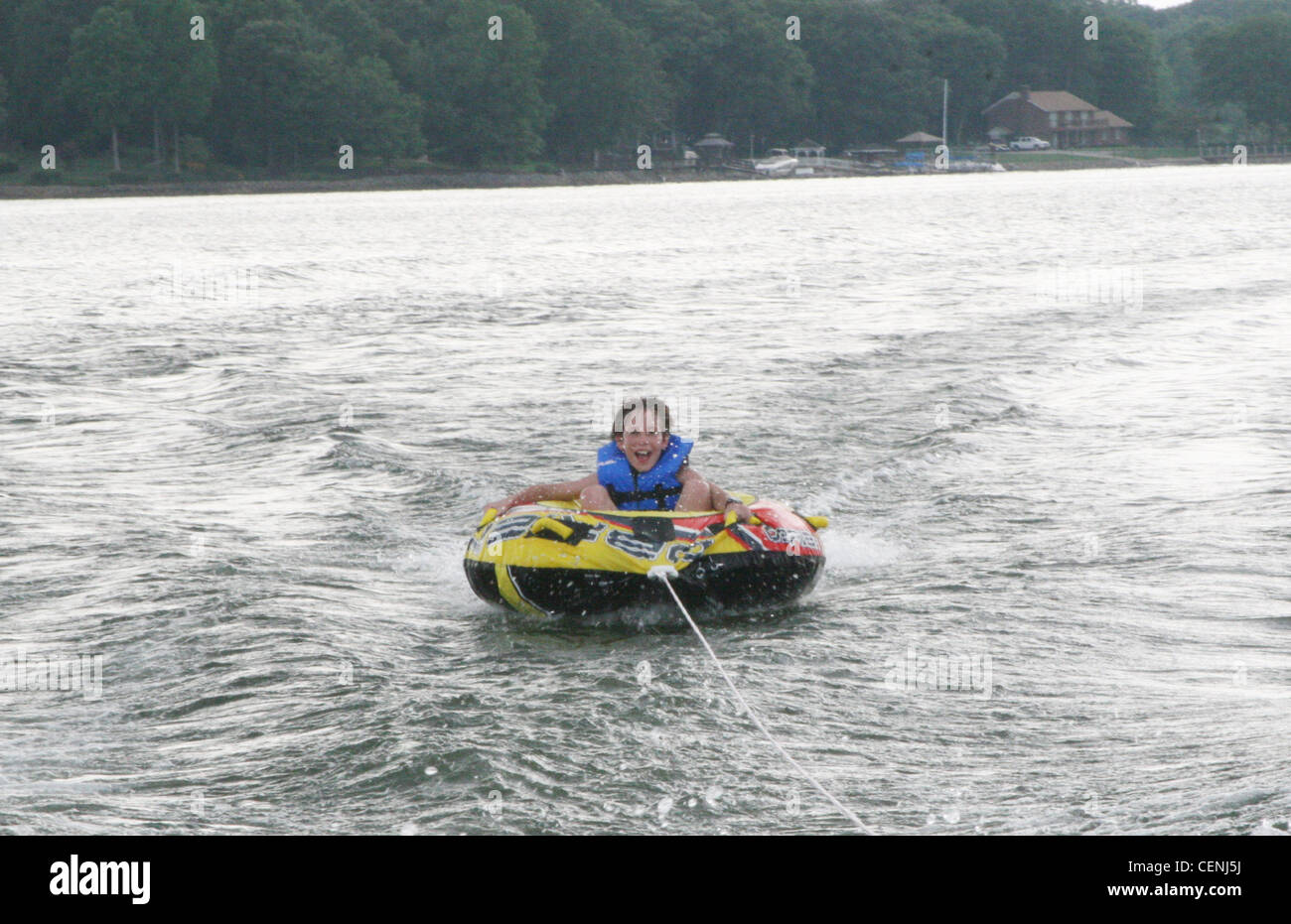 Ein junges männliches Kind, trägt eine blaue Schwimmweste, sitzen in einem towable Ski-Rohr in Wasser, lächelnd mit offenem Mund Stockfoto