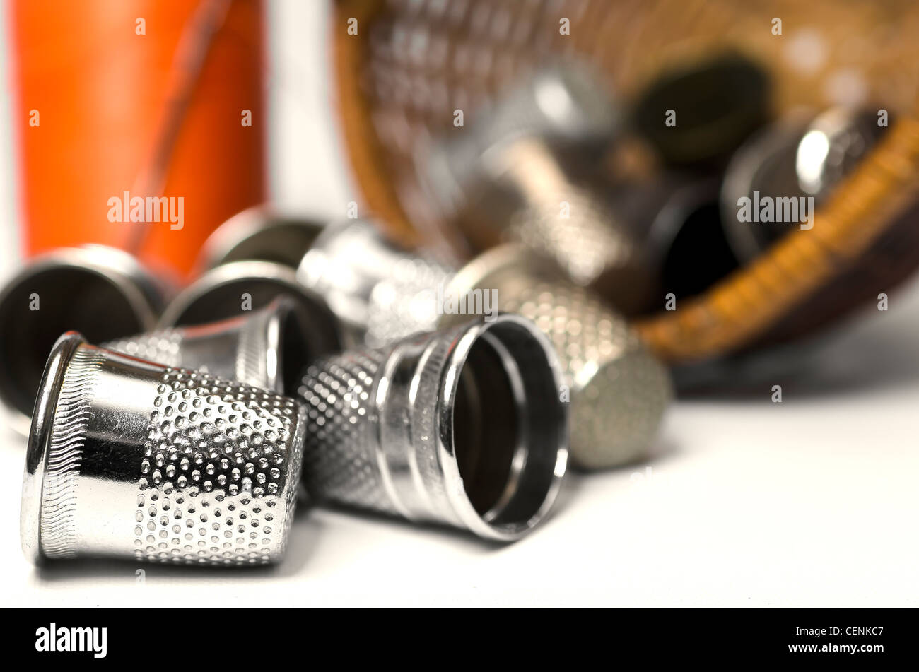 Fingerhüte verschüttet aus Korb mit Spule orange Faden und Nadel im Hintergrund. Stockfoto