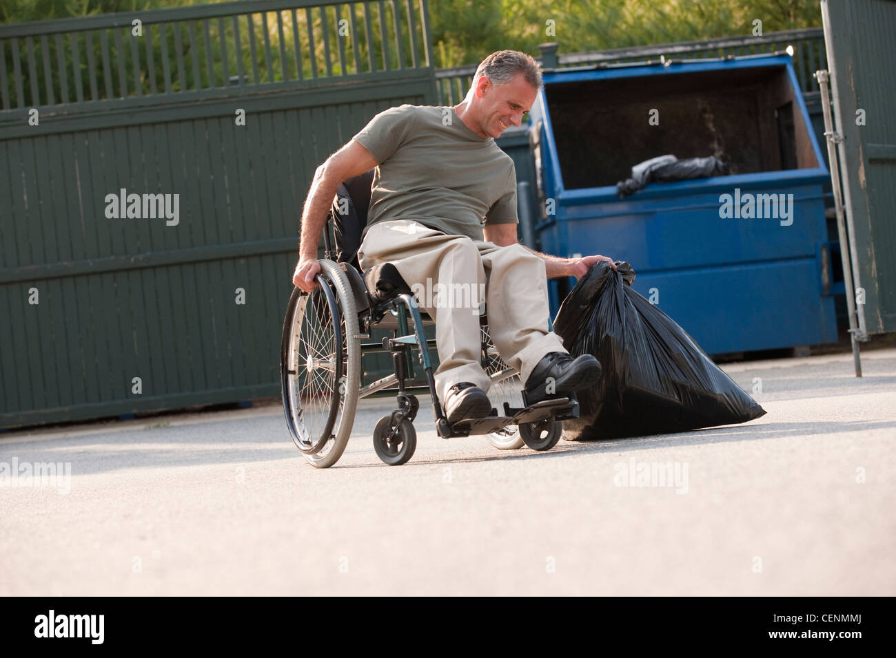 Mann im Rollstuhl zu schweren Müllsack zu bewegen versuchen Müllcontainer Stockfoto