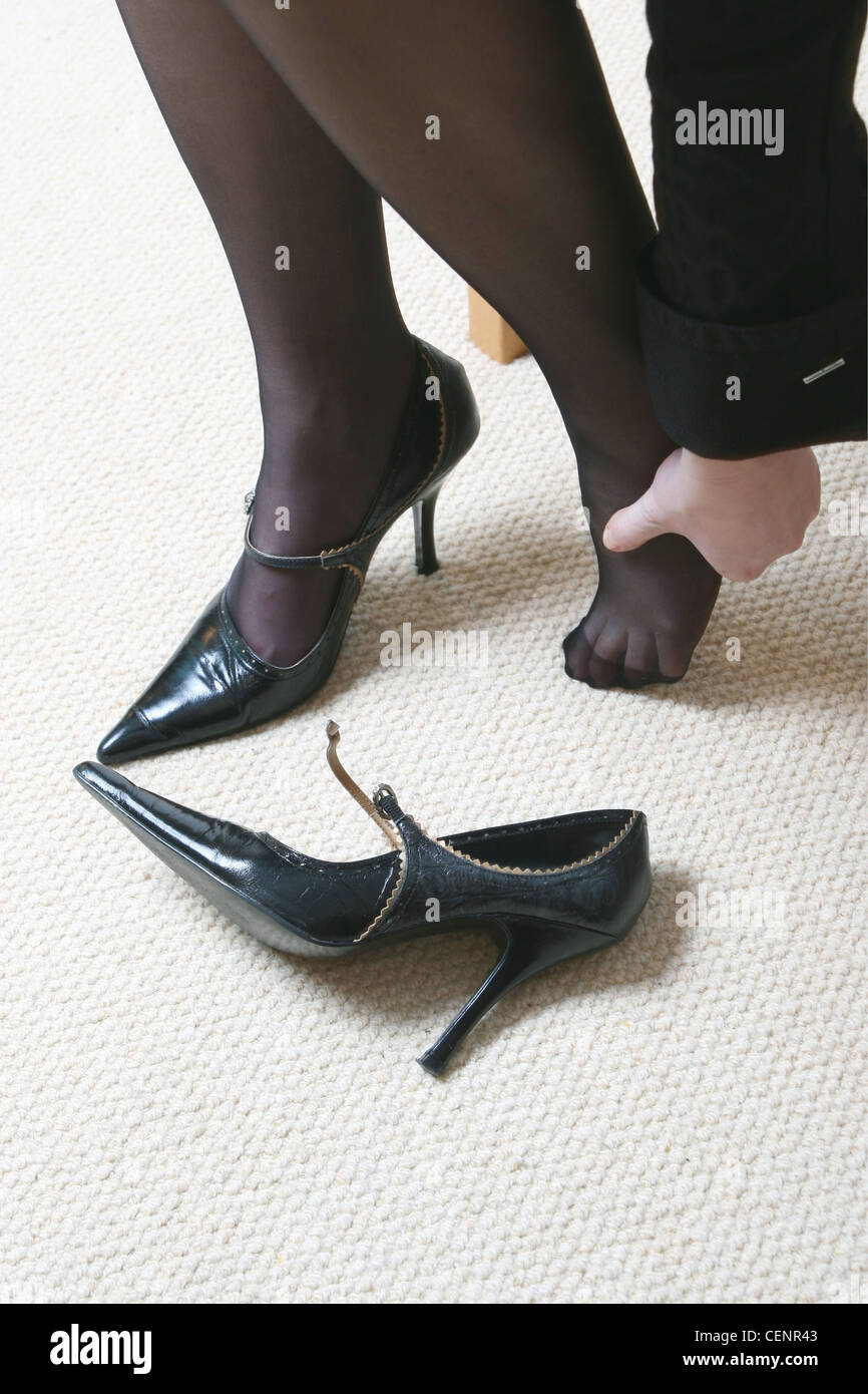 Frauen tragen schwarze Strumpfhose, hochhackige Schuhe spitz Zehen, Gurt und kleine Schnalle sitzen einen Schuh aus, reiben sie ihre Zehen Stockfoto
