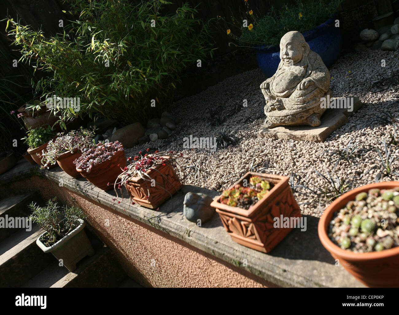 Blick auf einen orientalischen Garten Landschaftsbau, gekiester ein grauer Bereich eine fat Buddha-Statue in der Mitte kleine schwarze Lilyturf Stockfoto