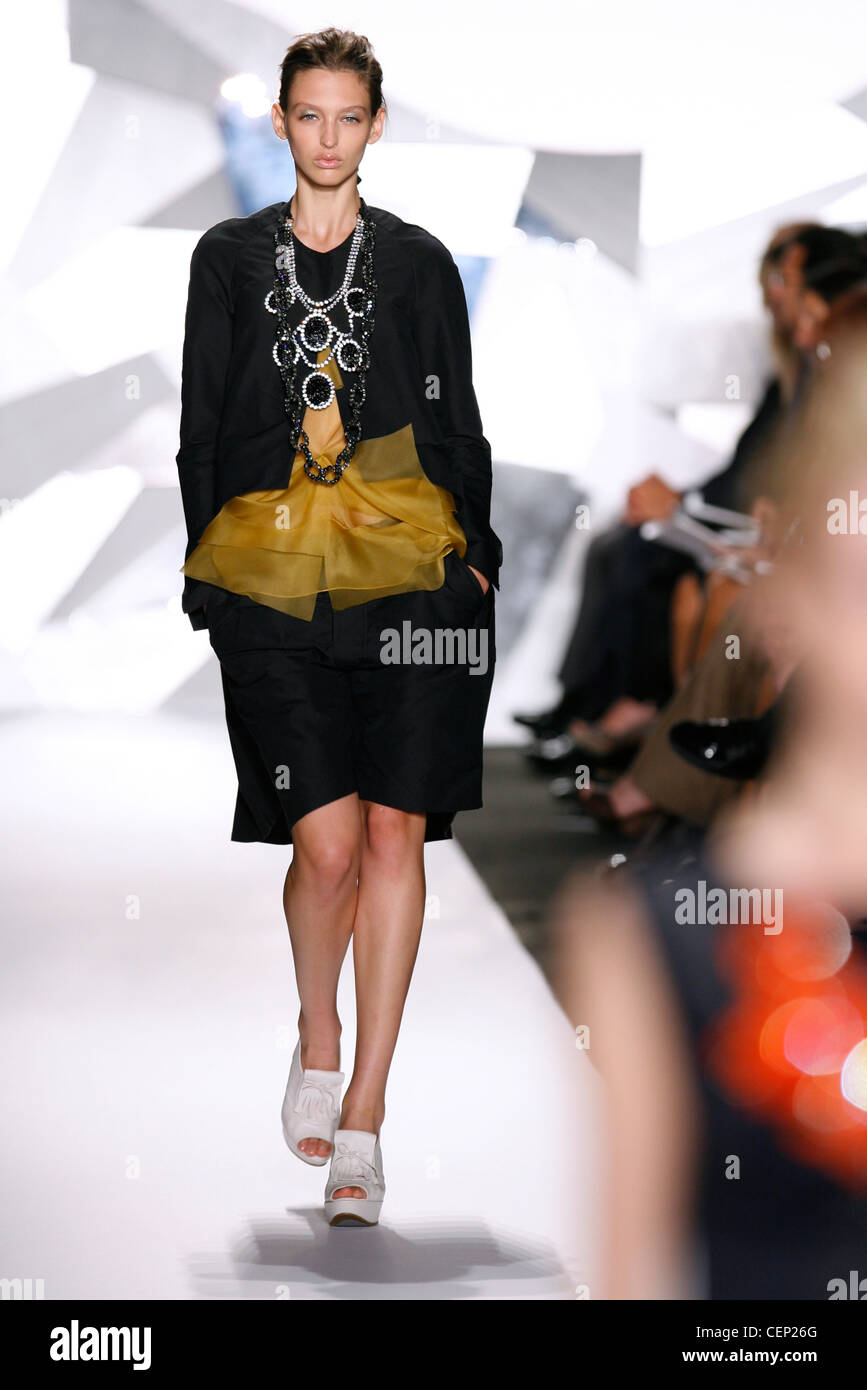 Vera Wang New York bereit, zwei Stück tragen Frühling Sommer schwarz beschnitten, Jacke und Rock, gold schiere Bluse, weiße Plateauschuhe Stockfoto