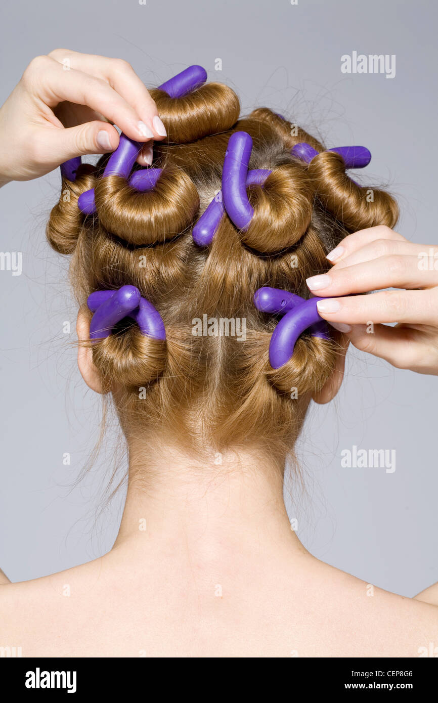 Rückansicht der Frau mit lange blonde Haare gewickelt auf lila Schaum  Lockenstäbe, Lockenwickler mit beiden Händen zu berühren Stockfotografie -  Alamy