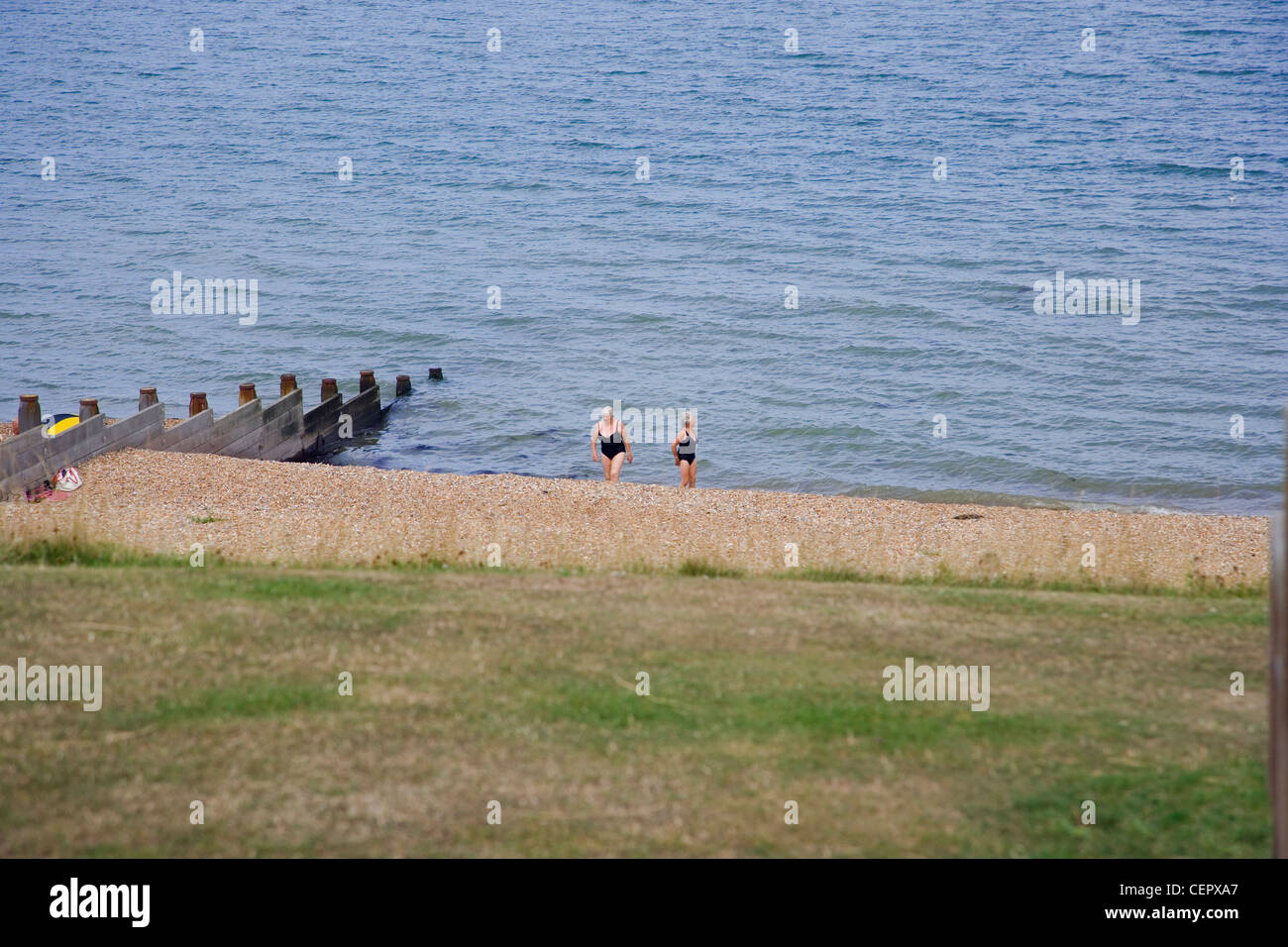Zwei Frauen in Baden Kostüme zu Fuß hinauf den Kiesstrand vom Meer entfernt in Whitstable. Stockfoto